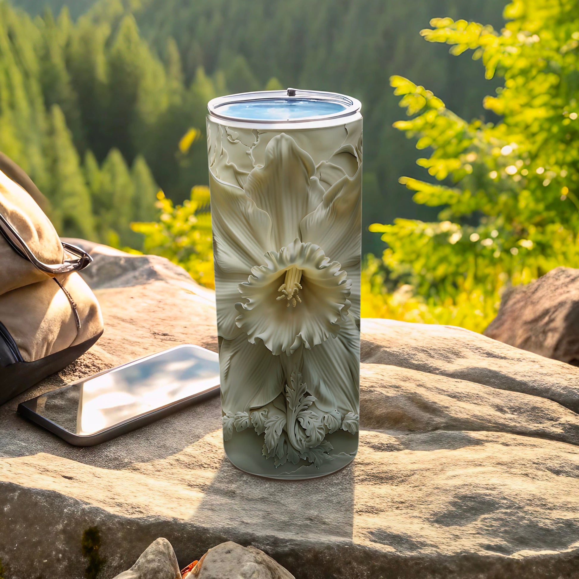 White floral design on a tall, cylindrical tumbler beside a backpack and phone.