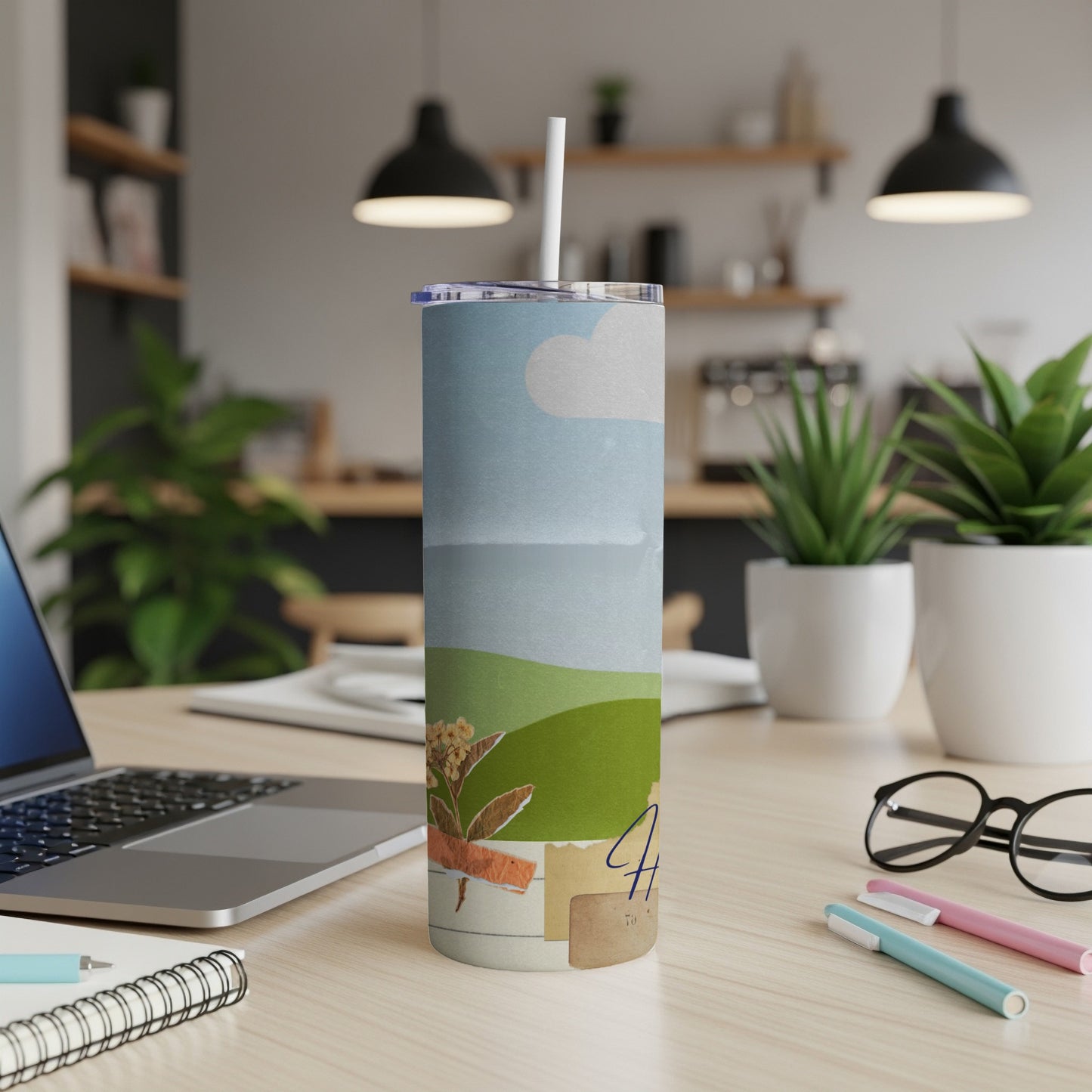 Tumbler with landscape art, straw, and a handwritten "Happy" on a desk.