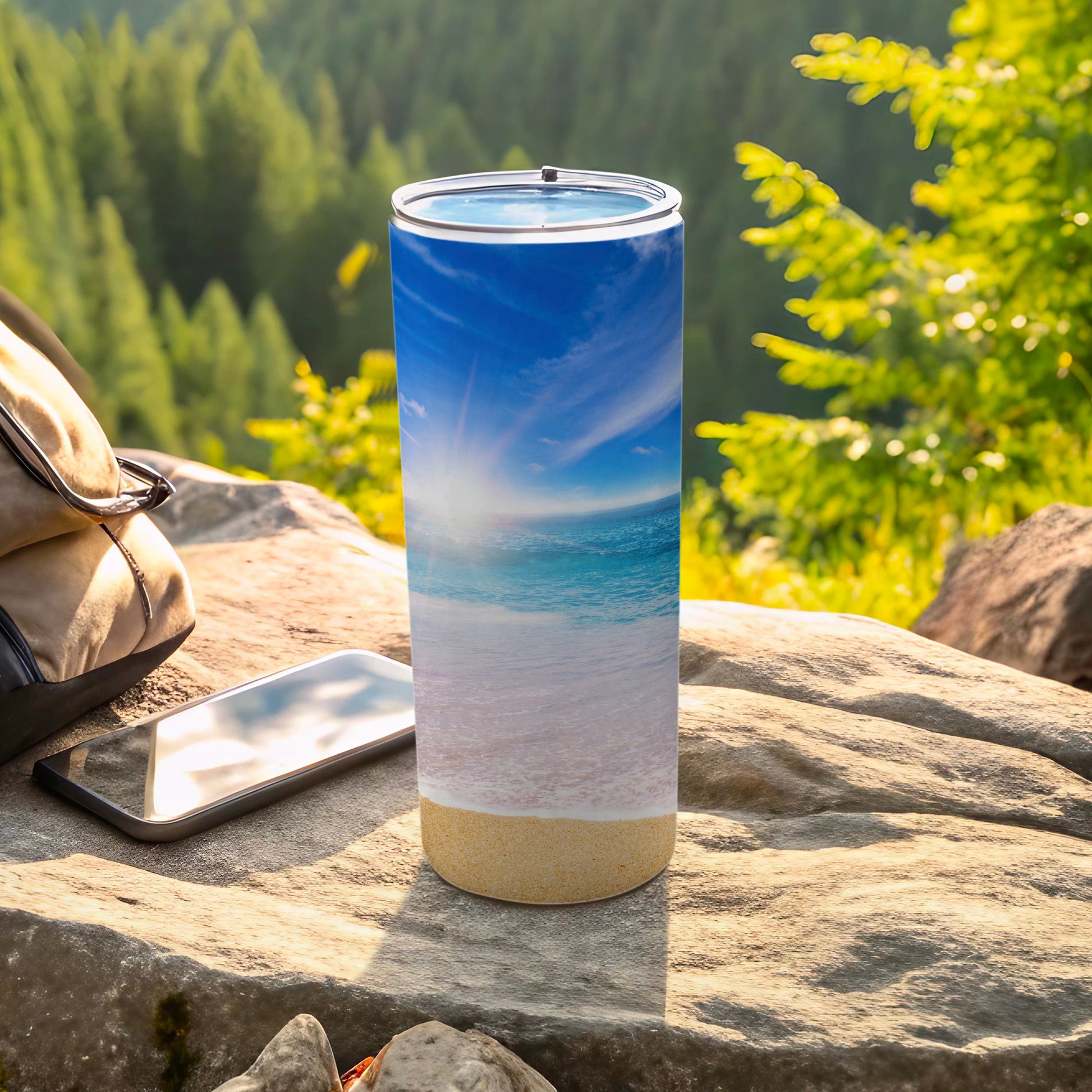 Tumbler with a beach scene and ocean waves, on a rocky surface.