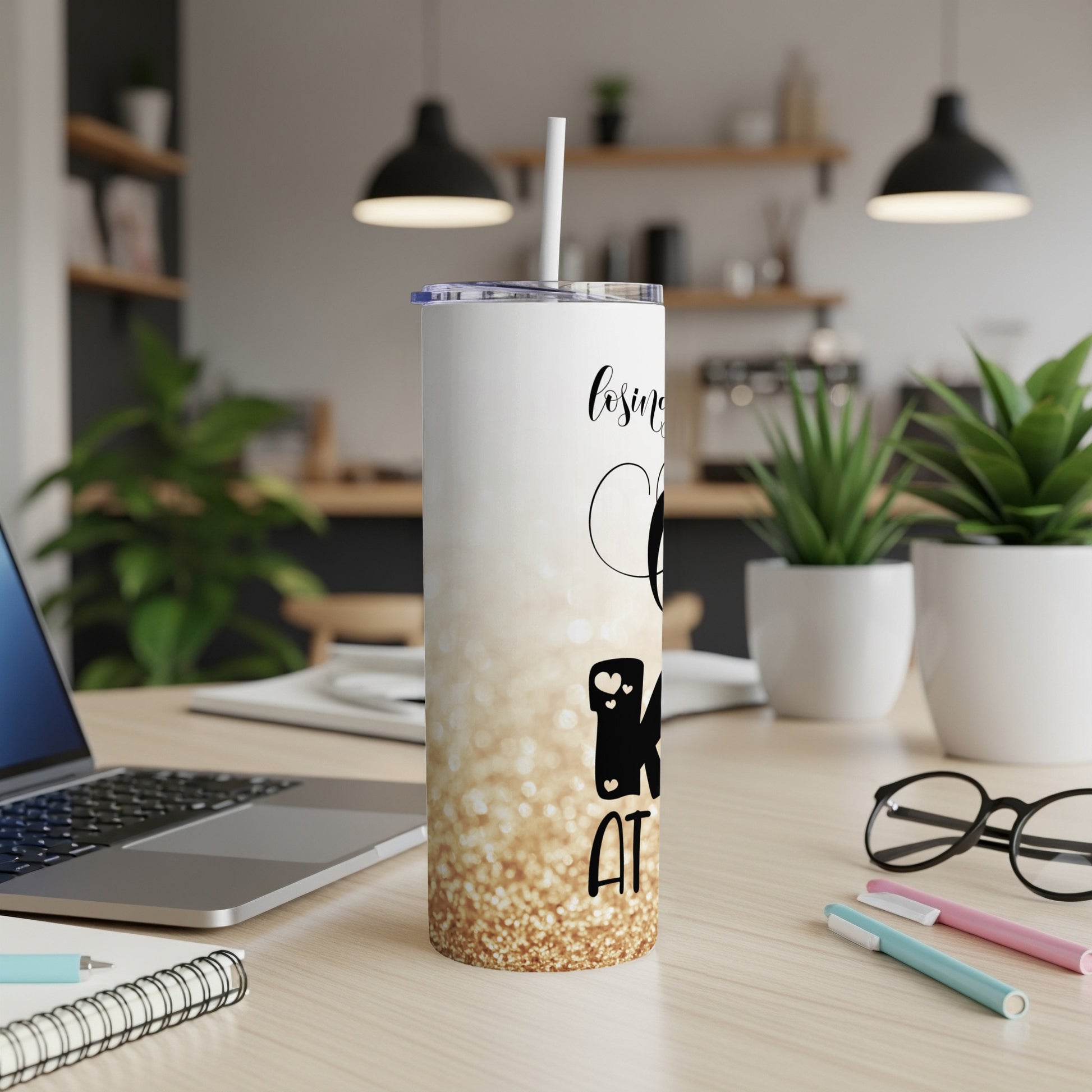 White tumbler with gold glitter, "Keepsake" text, and straw on a desk.