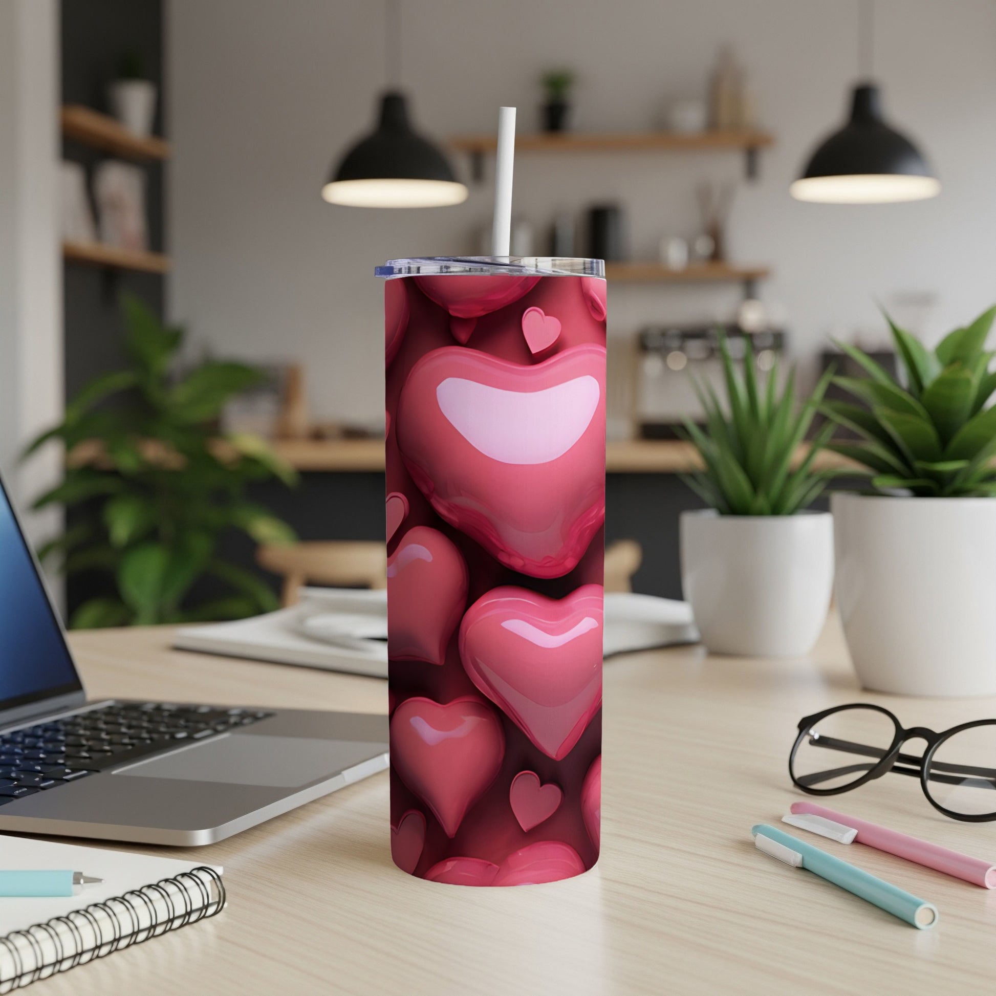 Pink heart pattern tumbler with straw on a wooden desk.