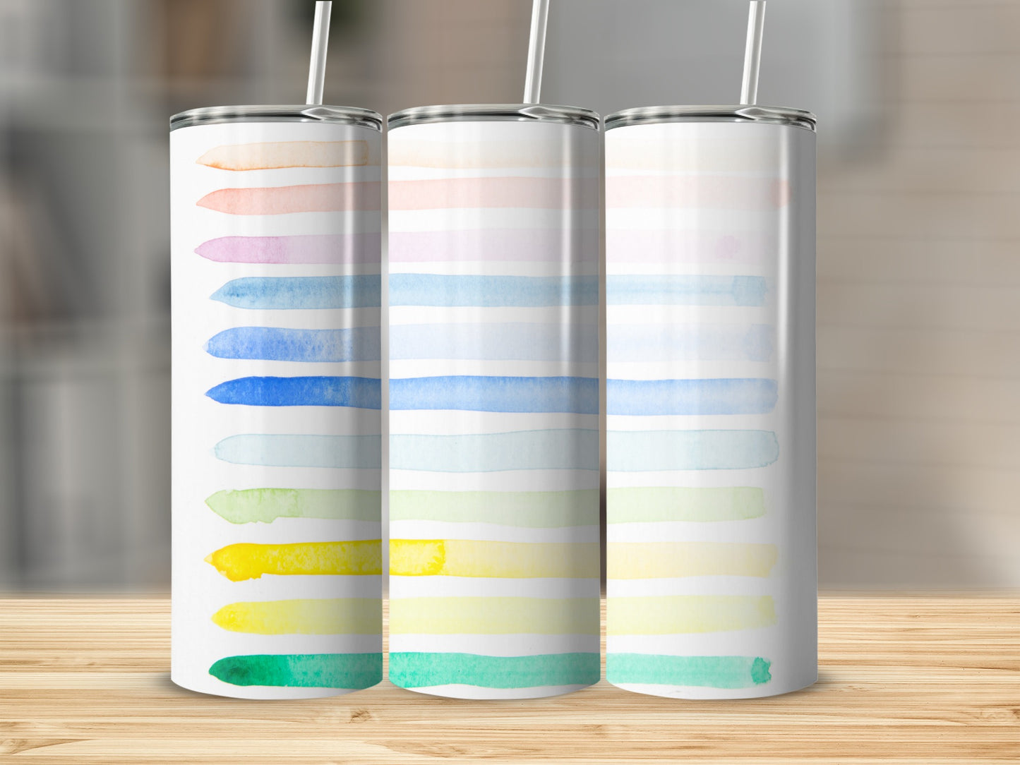 Three tumblers with watercolor stripes in pastel rainbow colors on a wooden surface.