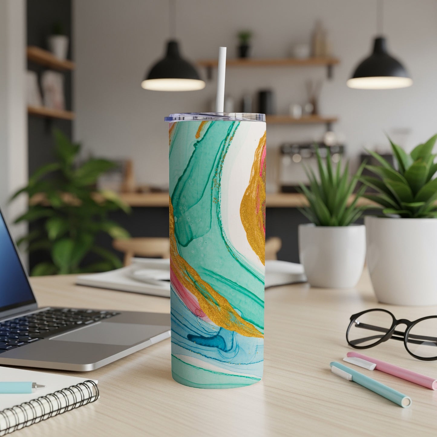 Teal, gold, and pink marbled tumbler with straw on a desk.