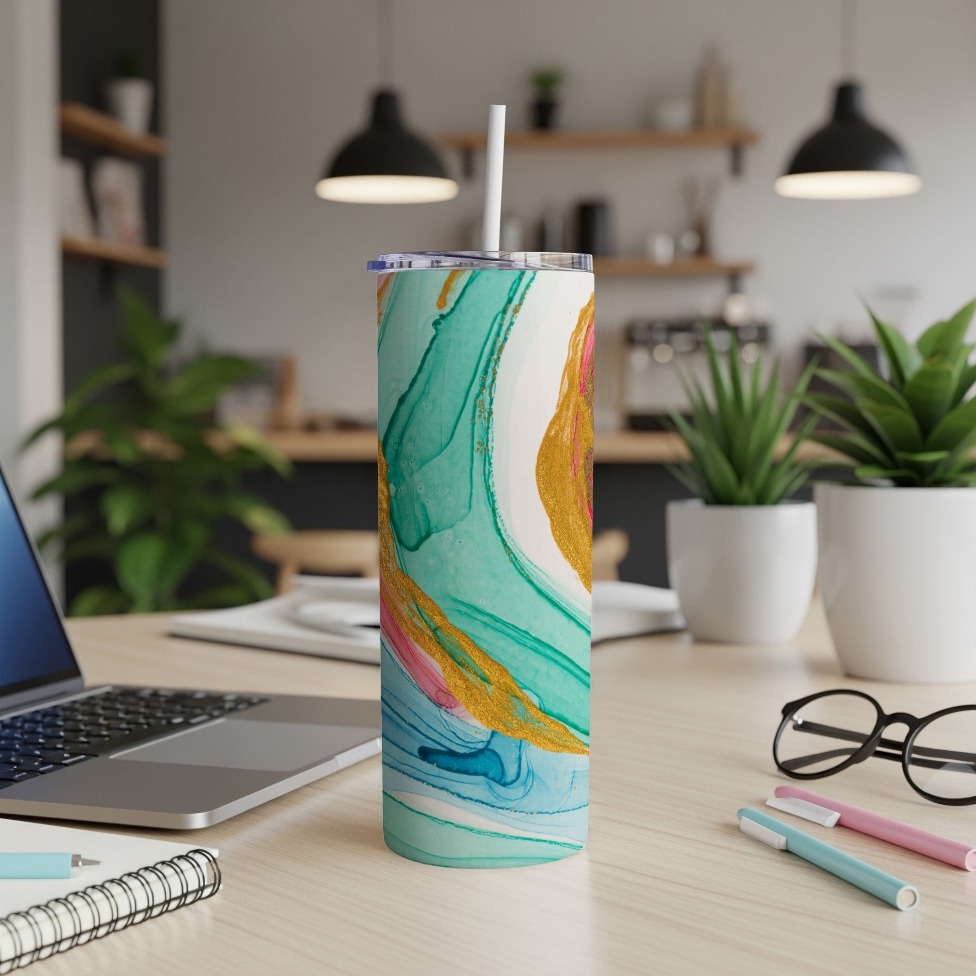 Teal, gold, and pink marbled tumbler with straw on a desk.