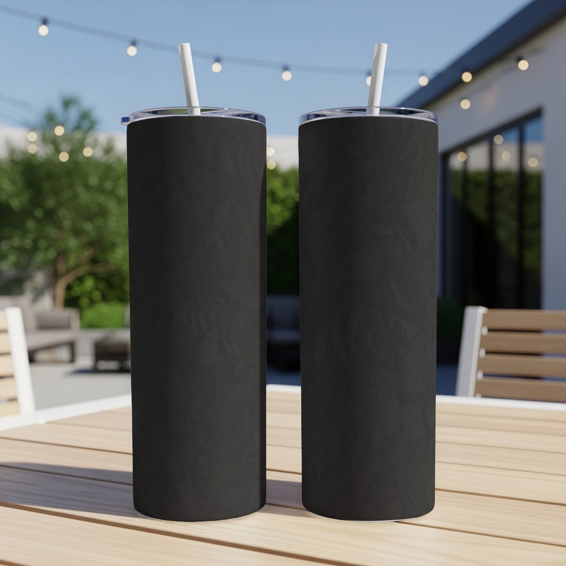 Two black tumblers with straws sit on a wooden table outdoors.