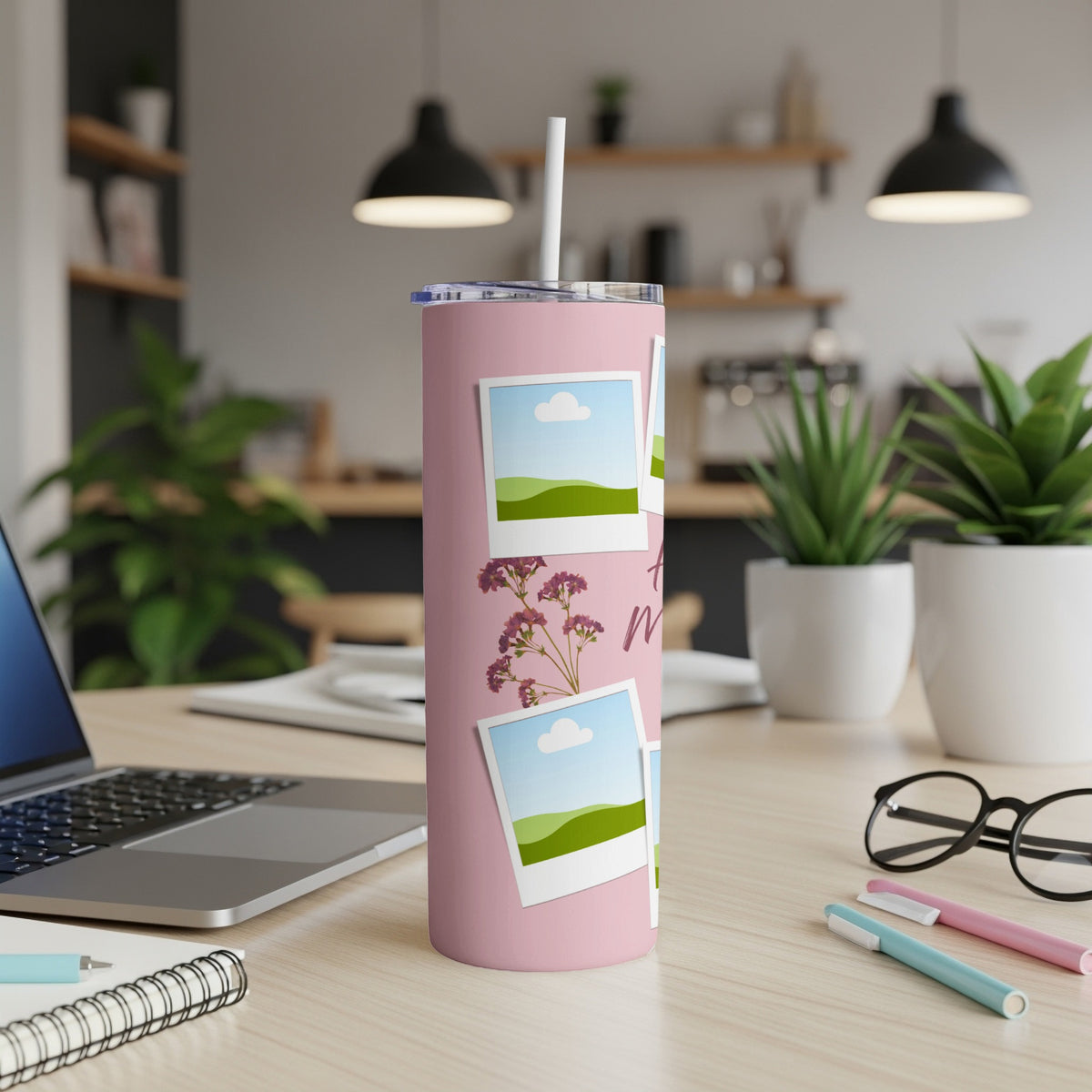 Pink tumbler with photo frames, floral design, and straw on a desk.