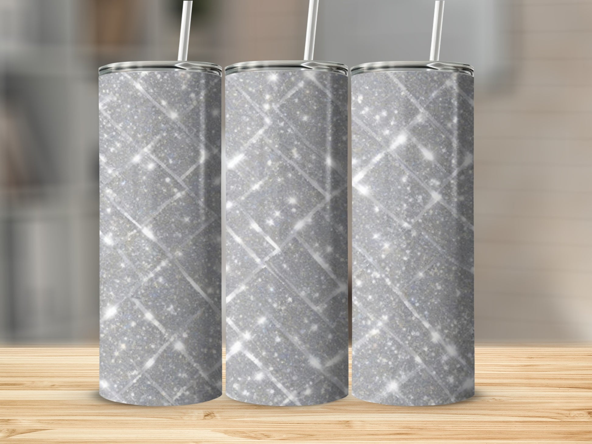 Three glittery silver tumblers with straws on a wooden surface.