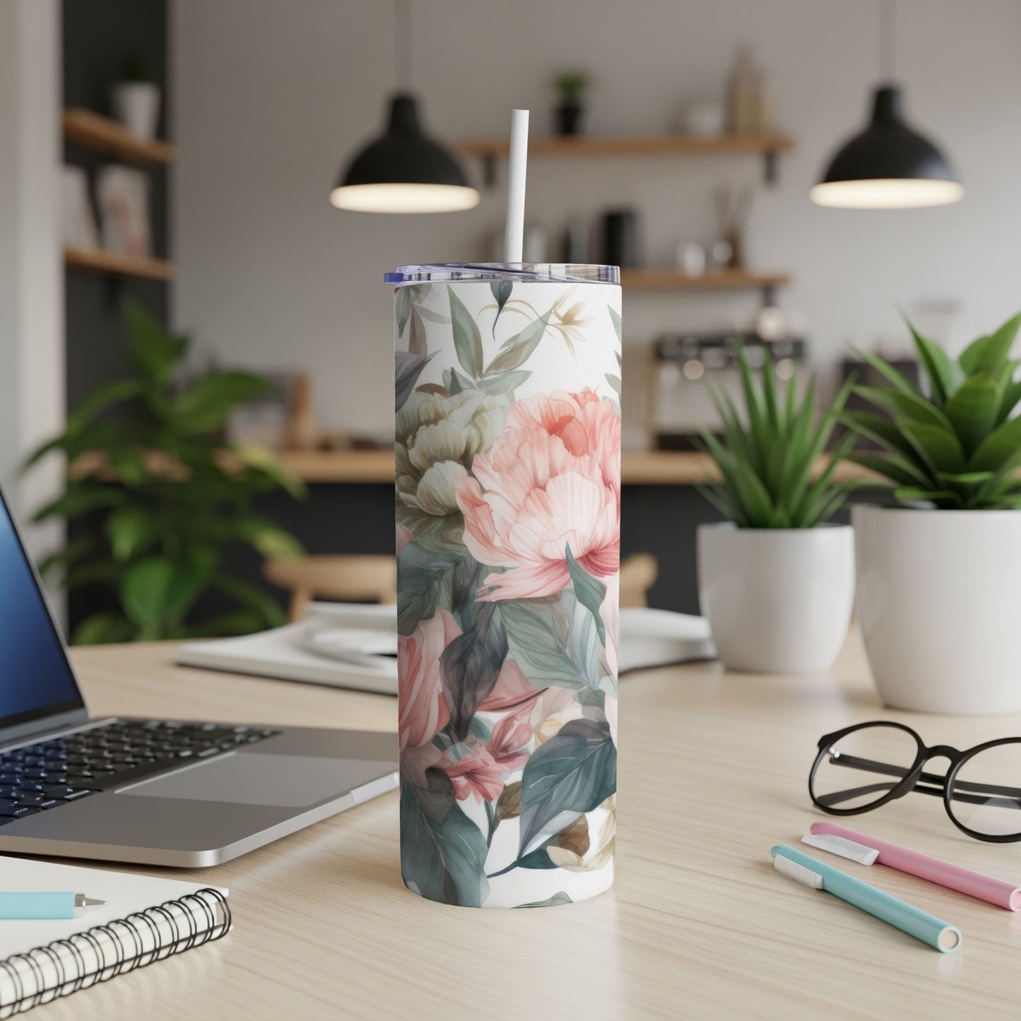 Floral print tumbler with straw on a desk with a laptop and pens.