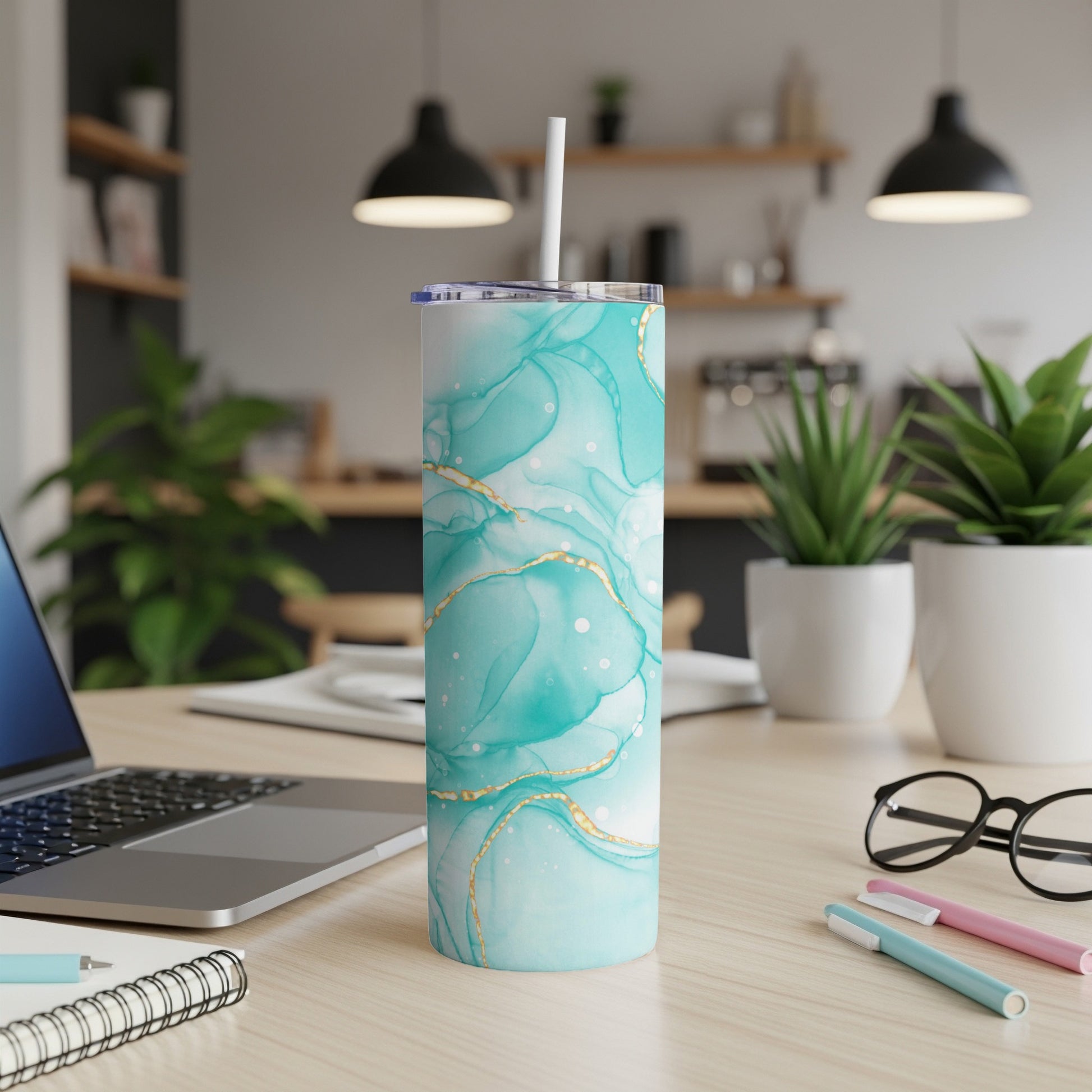 Teal and gold marble pattern skinny tumbler with white straw on a desk.