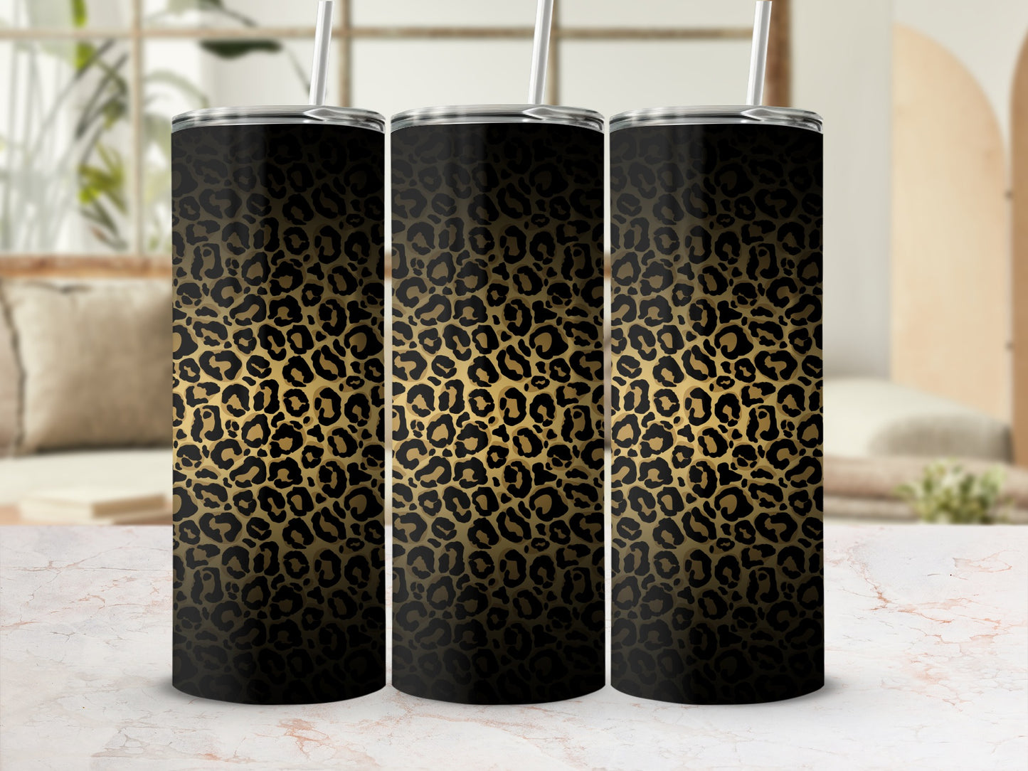 Three black and gold leopard print tumblers with straws on a marble surface.