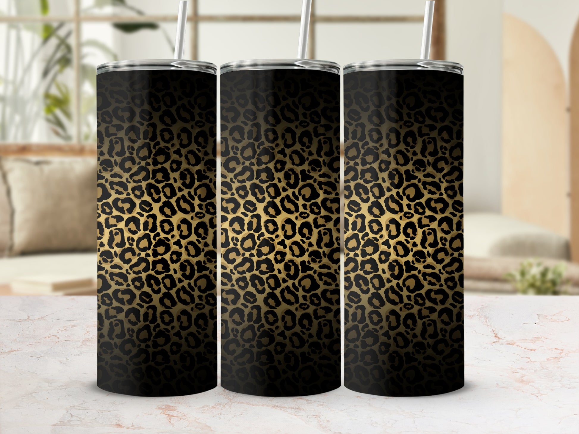 Three black and gold leopard print tumblers with straws on a marble surface.