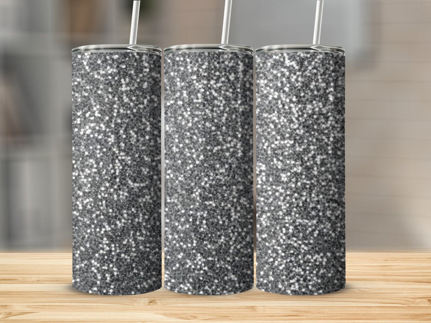 Three silver glitter tumblers with straws stand on a wooden surface.