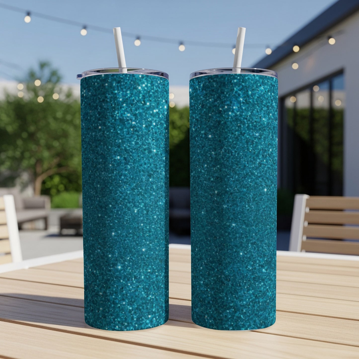Two teal glitter tumblers with straws stand on a wooden table outdoors.
