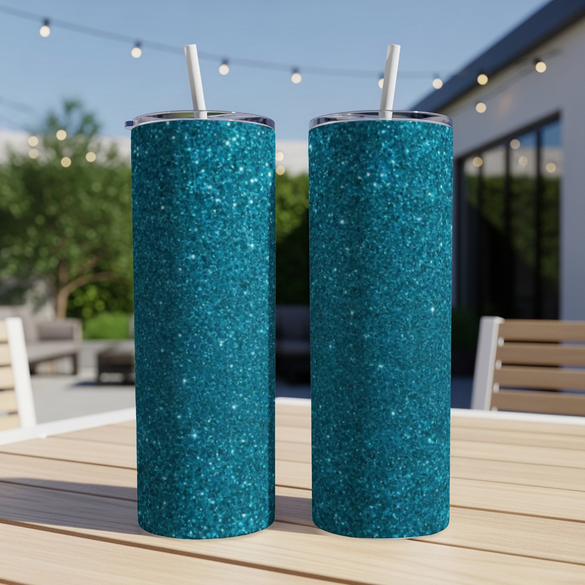Two teal glitter tumblers with straws stand on a wooden table outdoors.