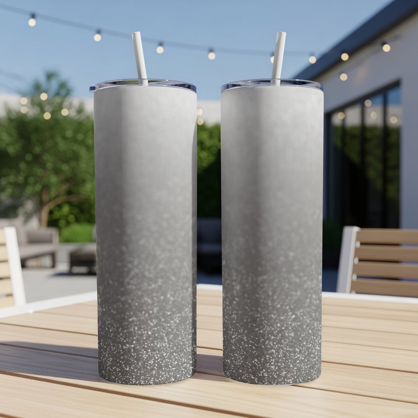 Two tall, silver glitter tumblers with straws on a wooden table.