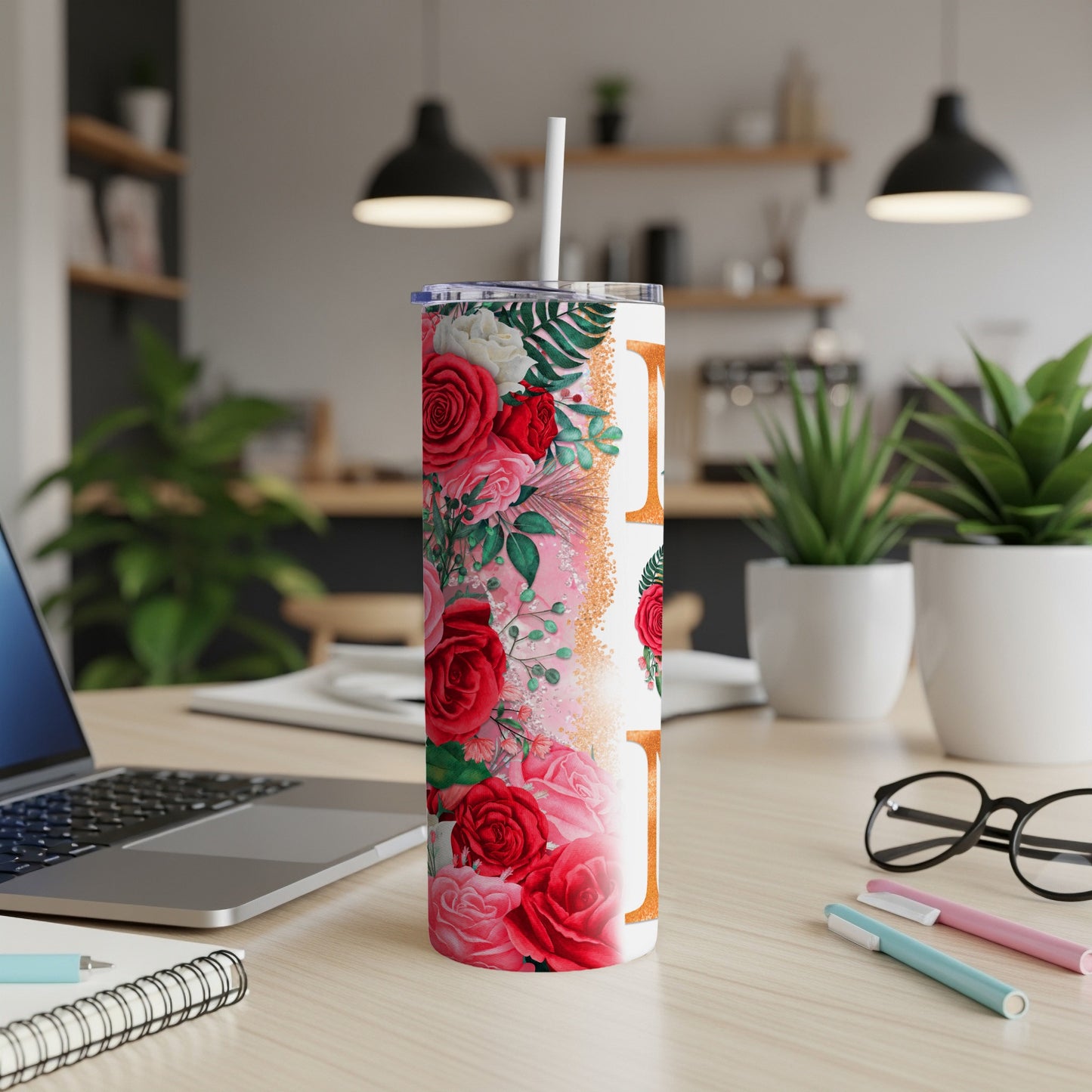 Floral tumbler with straw on a desk next to a laptop.