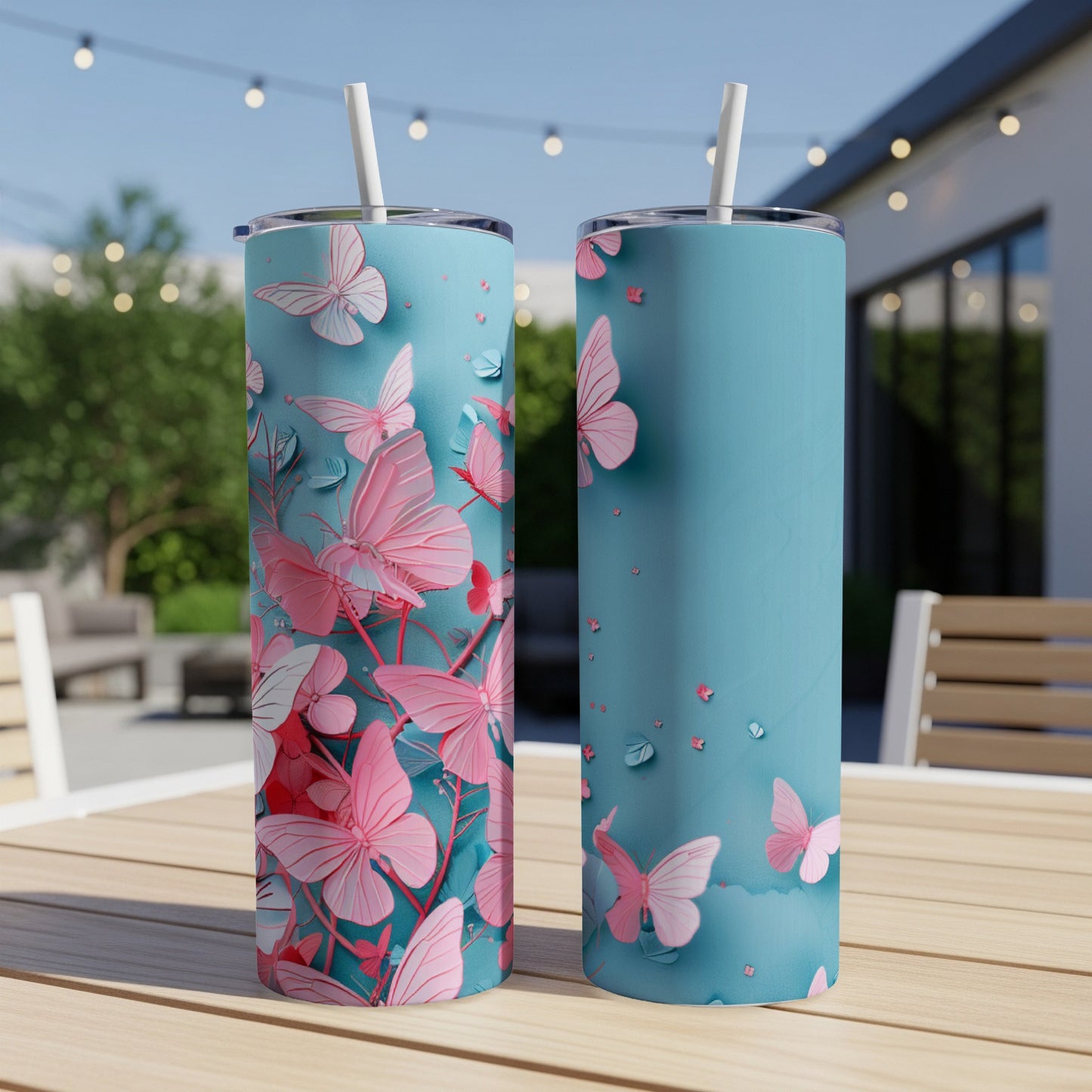 Two teal tumblers with pink butterflies and floral designs on a patio table.