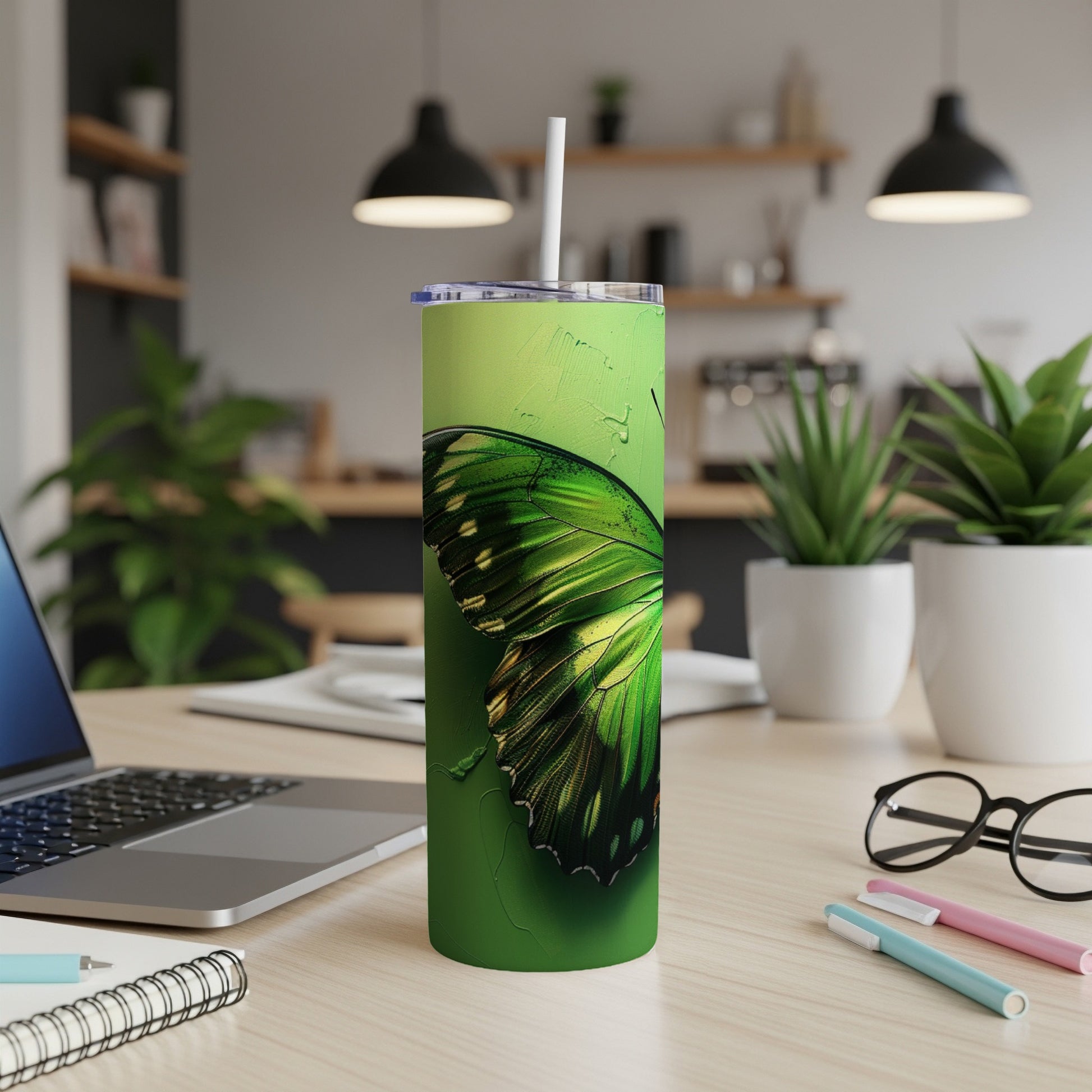 Green butterfly tumbler with straw on a desk with a laptop.