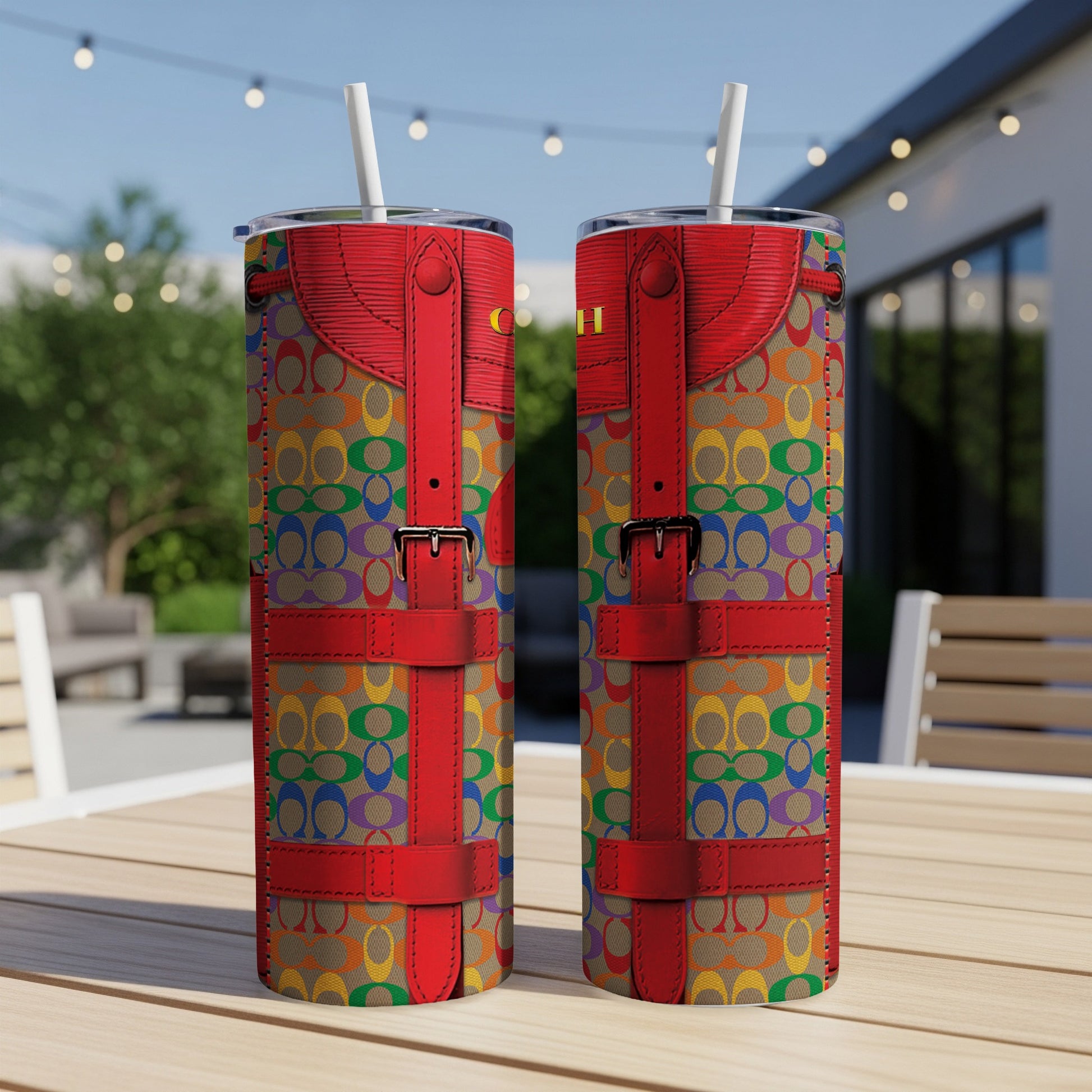 Two tumblers with rainbow logo pattern and red strap accents on a wooden table.