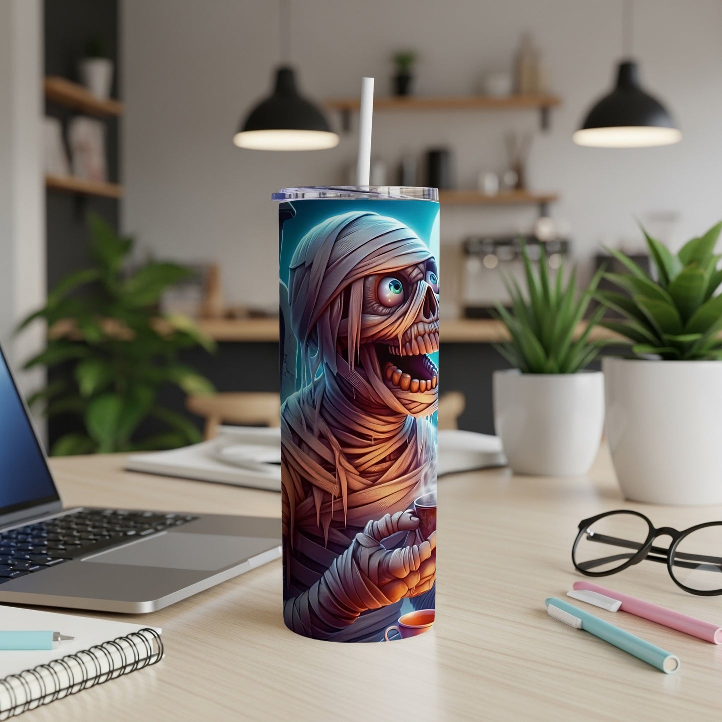 Mummy tumbler with straw on desk next to laptop, notebook, and pens.