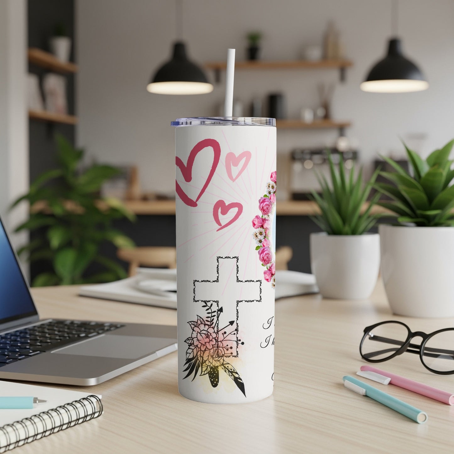 White tumbler with hearts, cross, flowers, and text on a desk.