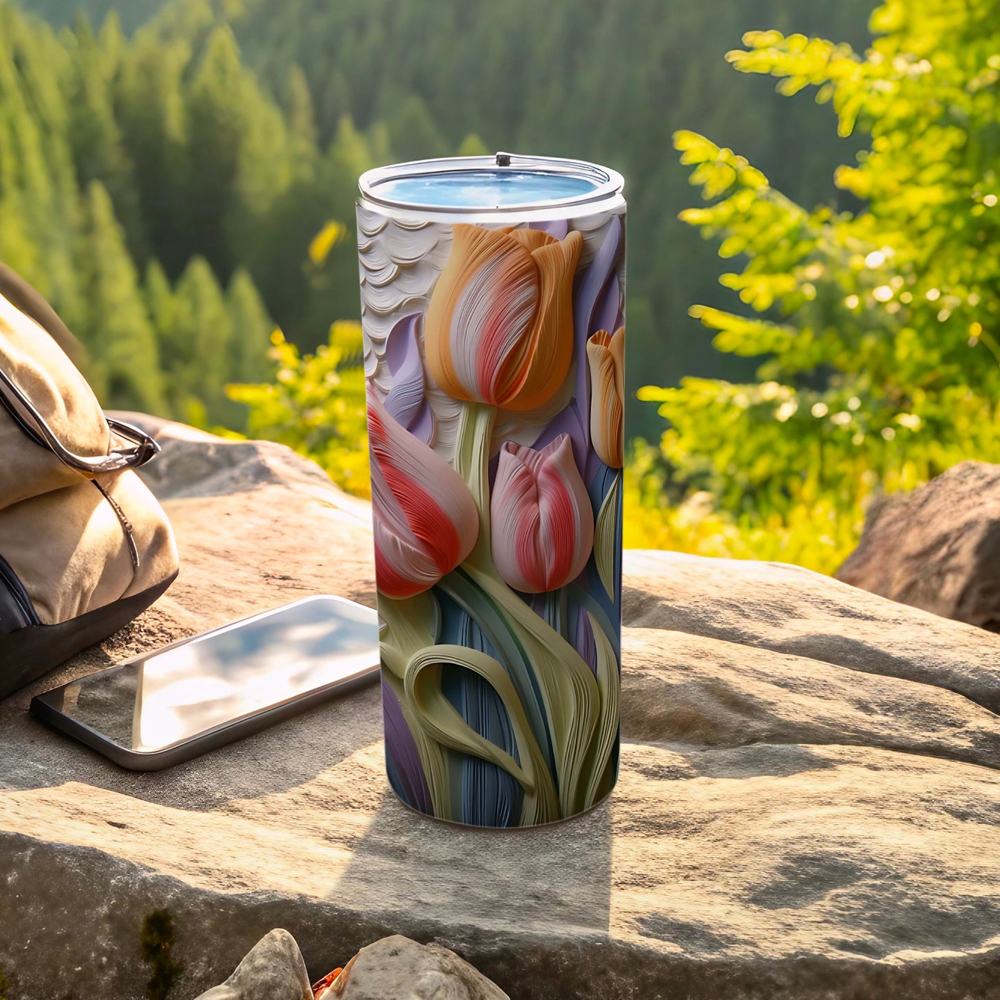 Tumbler with tulips design on rock with backpack and phone.