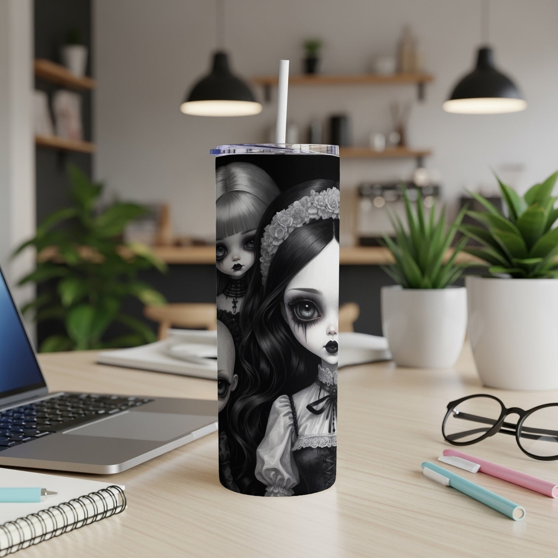 Gothic doll characters on a tumbler with a straw, on a desk.