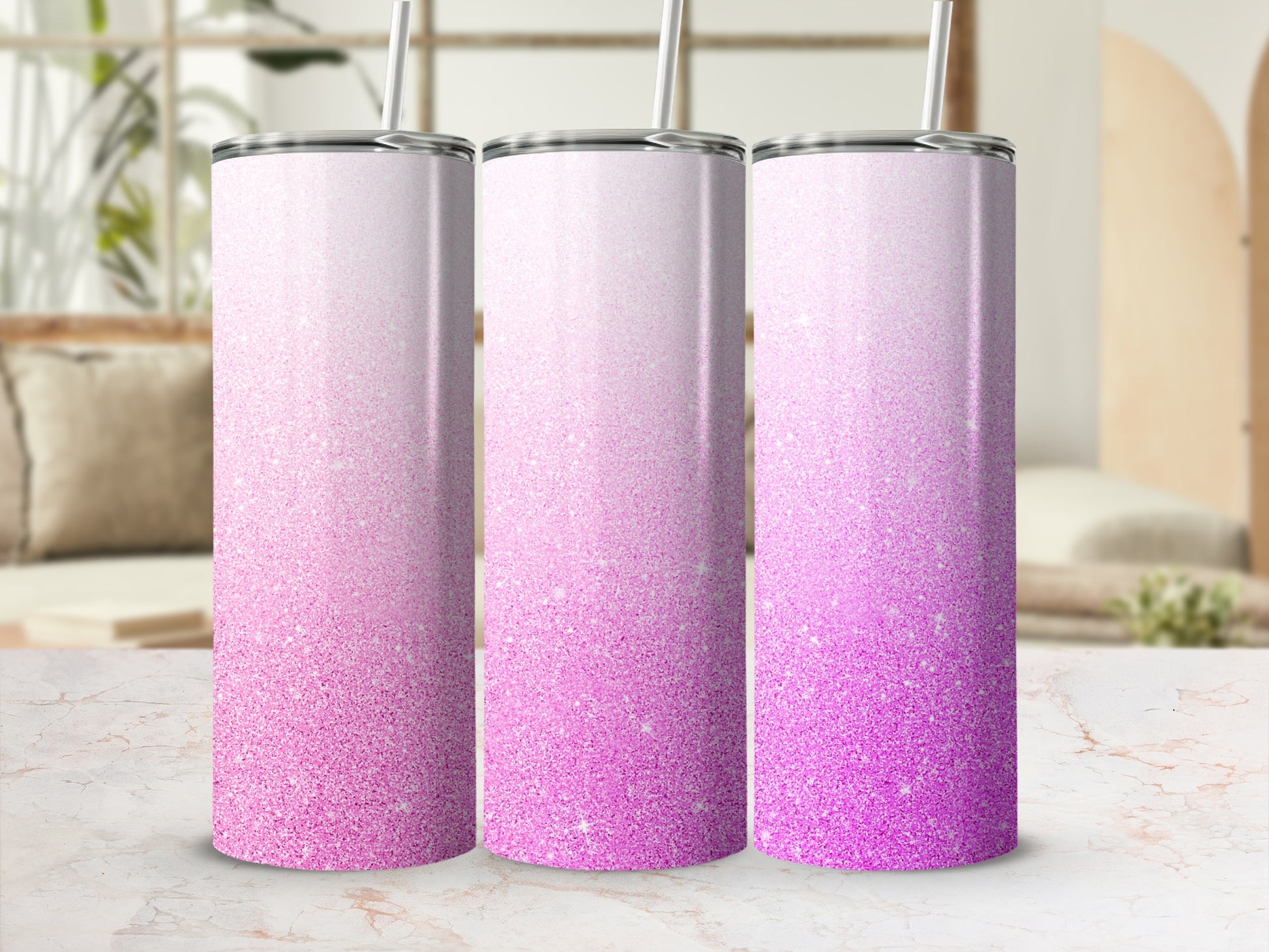 Three pink glitter ombre tumblers with straws displayed on a marble countertop.