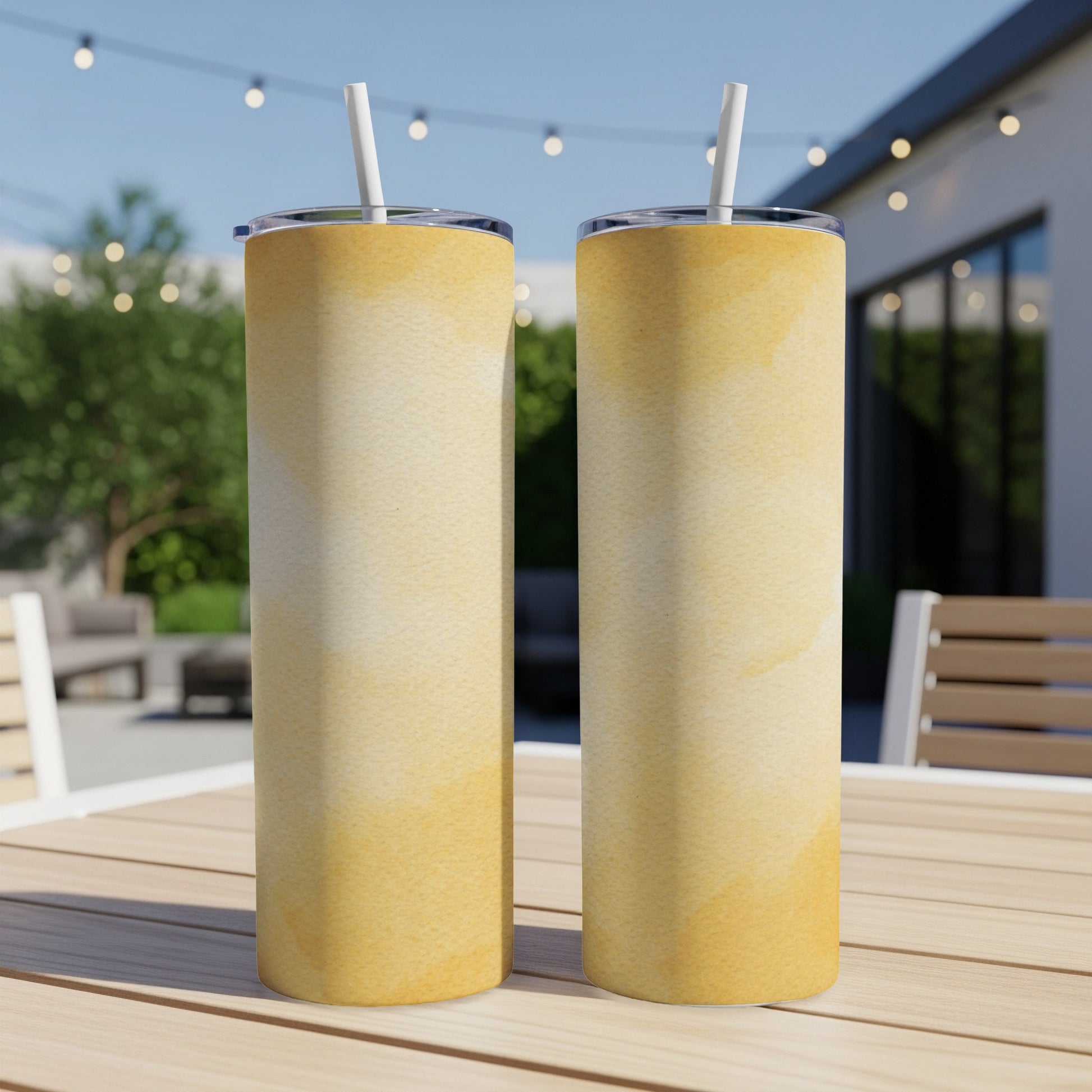 Two yellow watercolor tumblers with straws on a table outdoors.