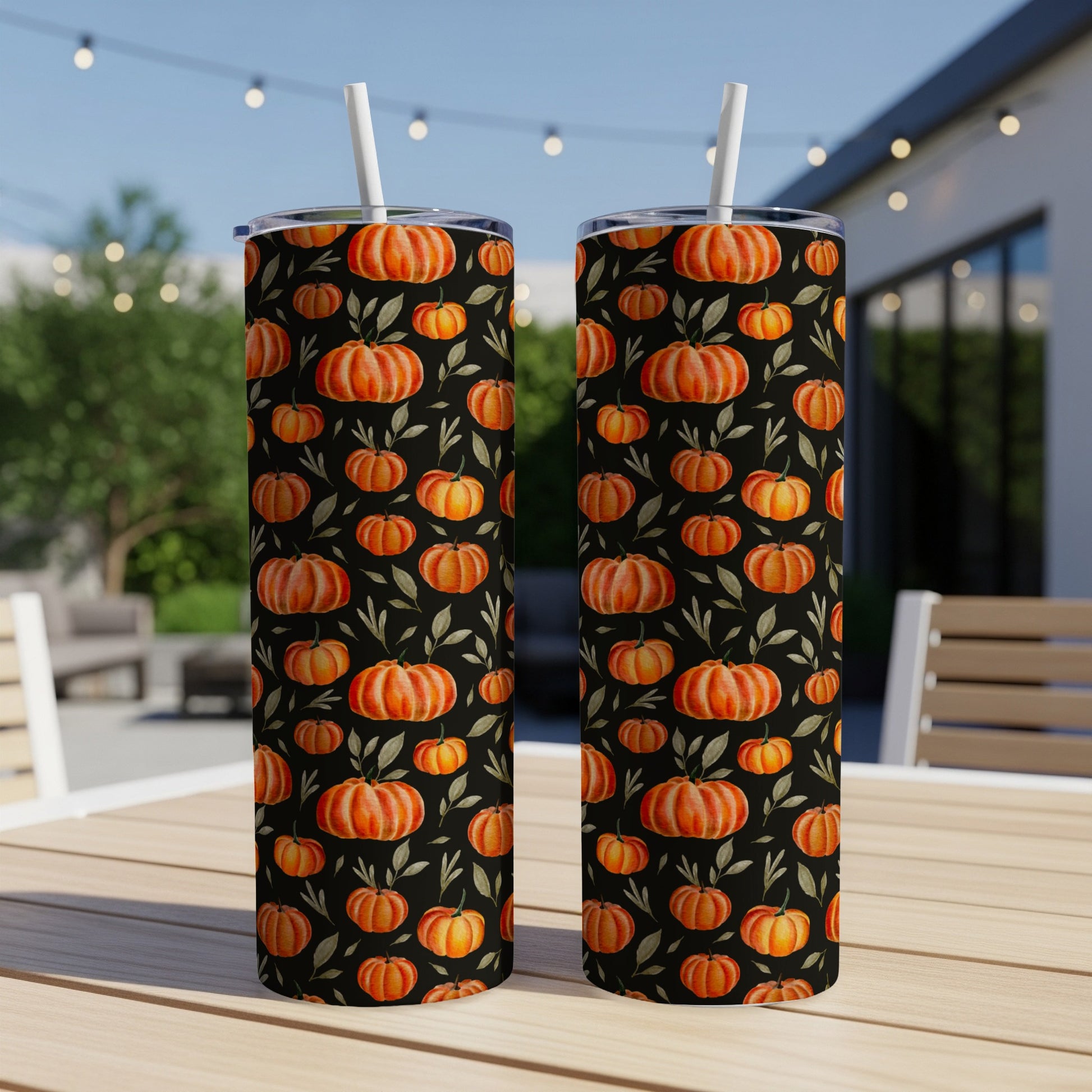 Two tall tumblers with a pattern of pumpkins and leaves on a dark background.