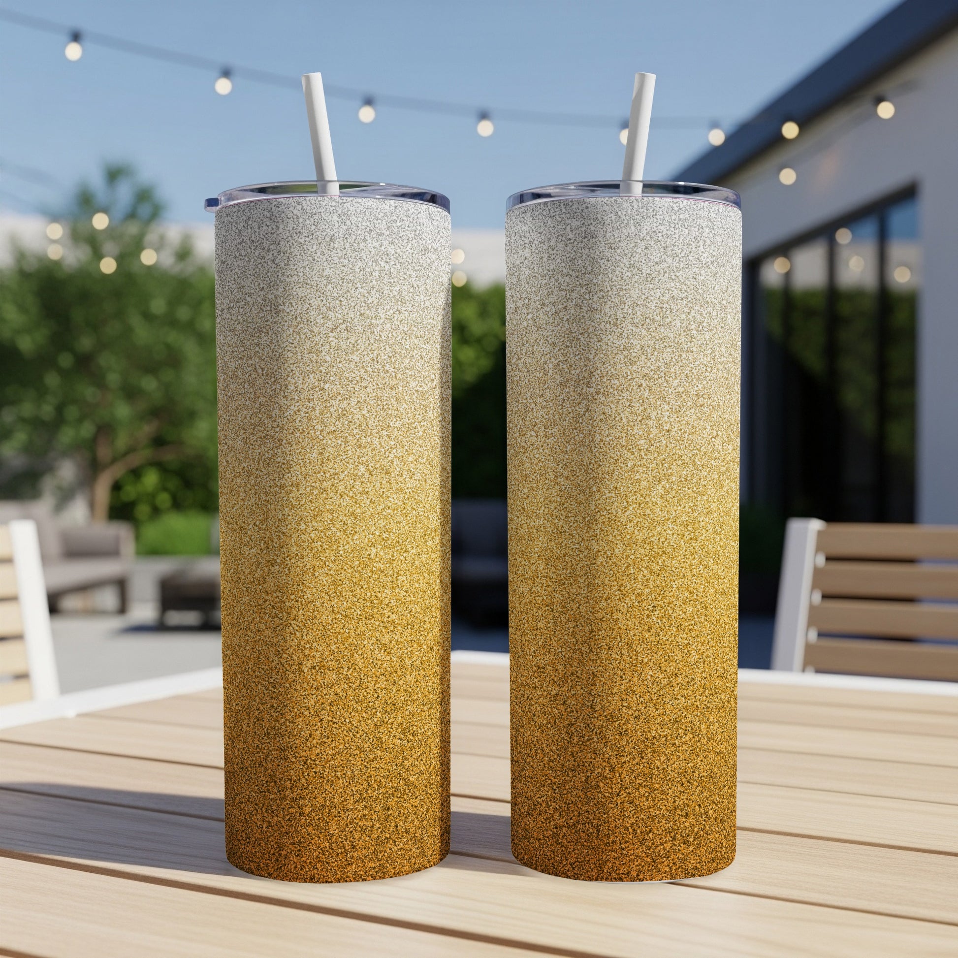 Two tall tumblers with a gold to white gradient glitter design and straws.