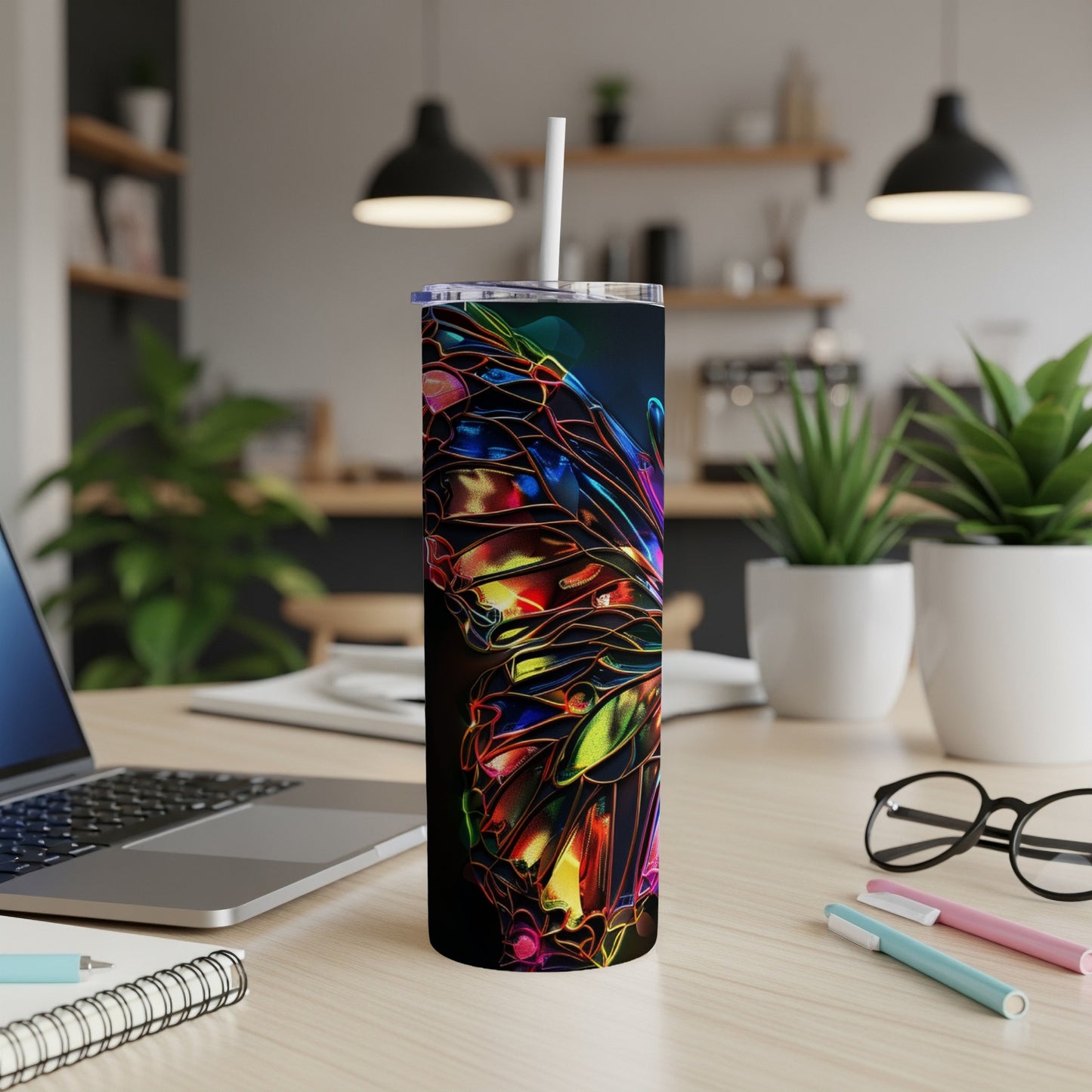 Colorful abstract butterfly pattern on a dark tumbler with straw, on a desk.
