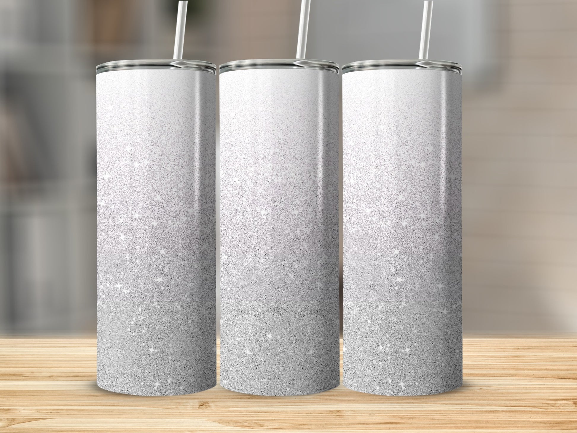 Three silver glitter ombre tumblers with straws on a wooden surface.