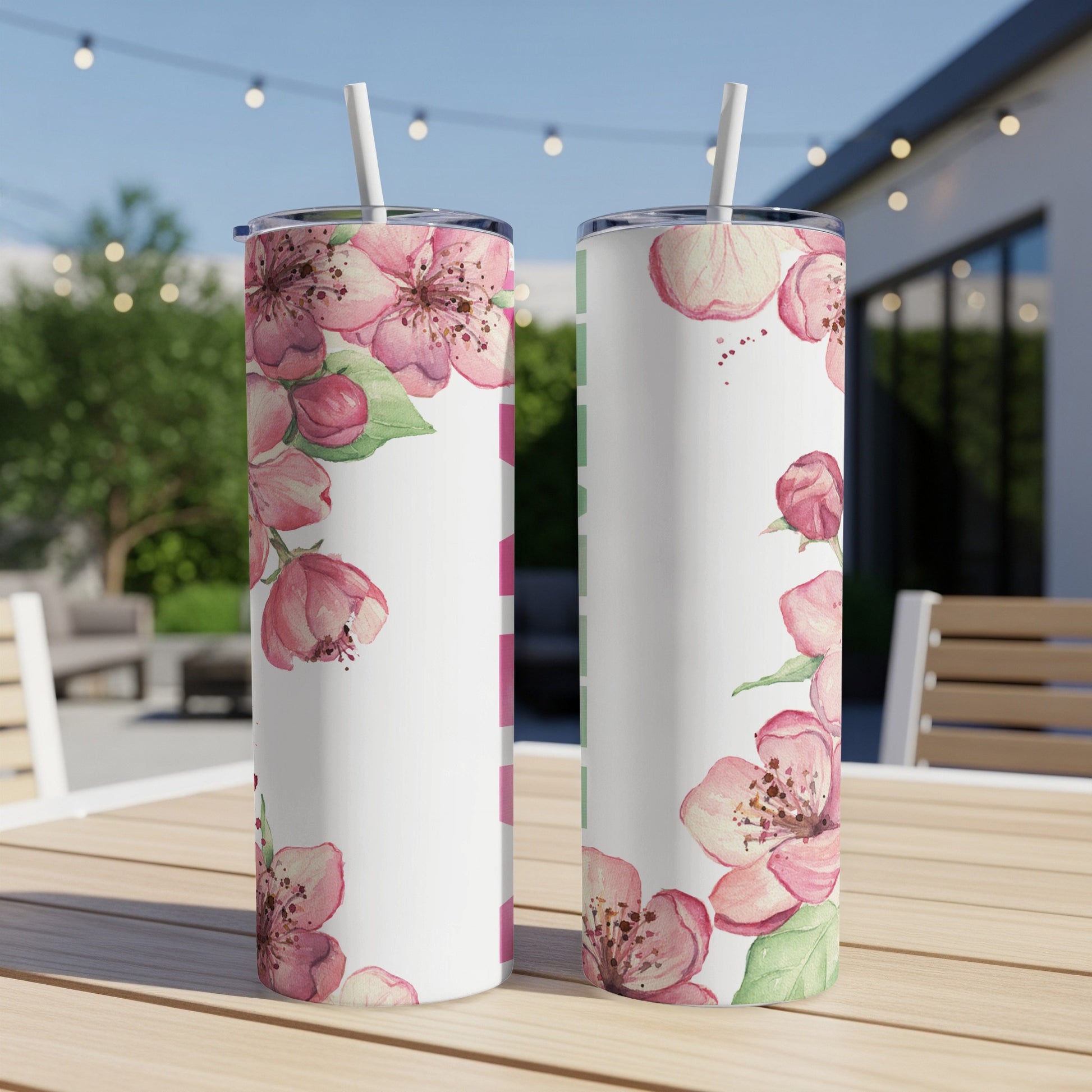 Two white tumblers with pink floral designs sit on a wooden table outdoors.