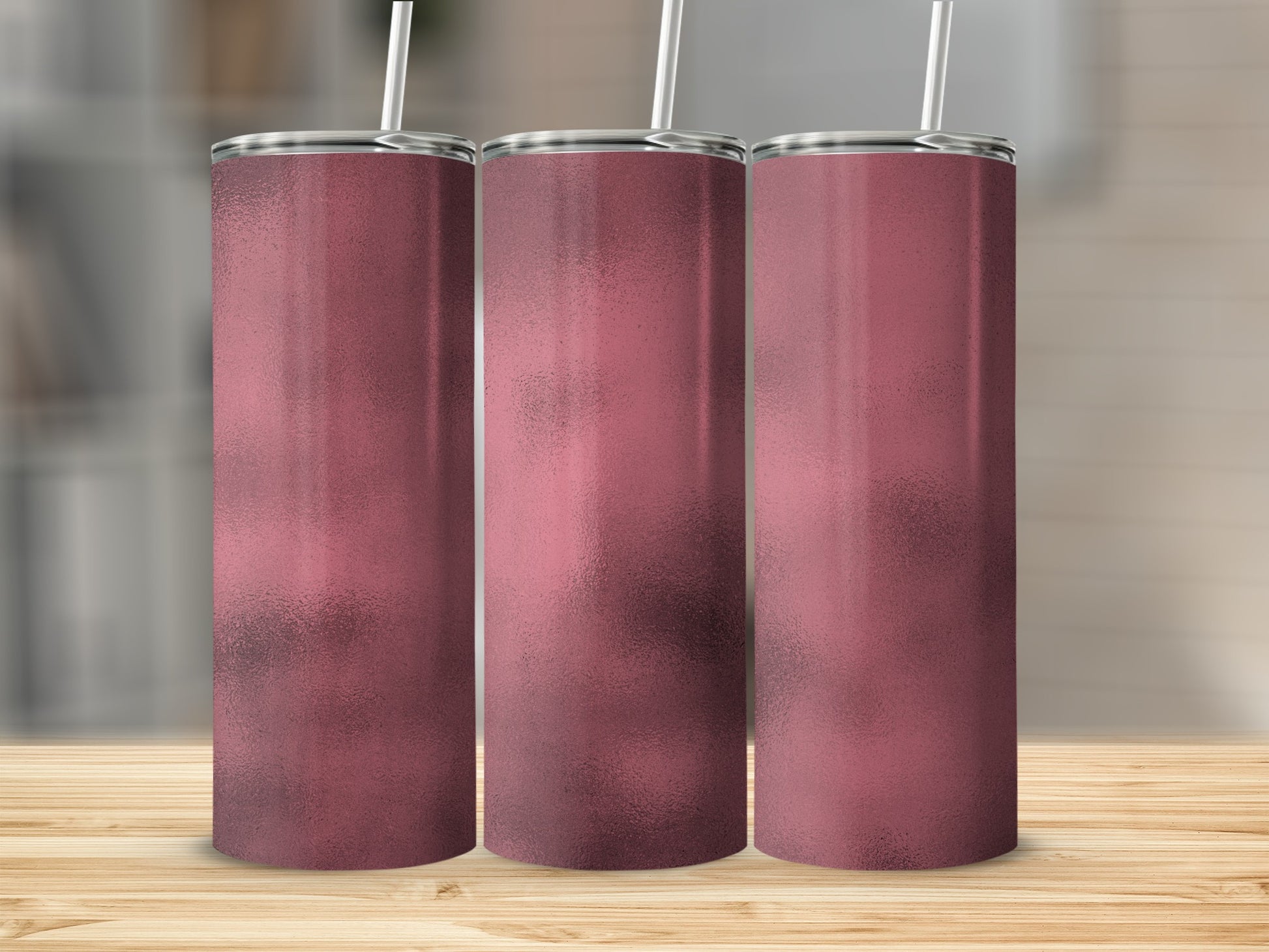 Three rose gold tumblers with straws stand on a wooden surface.