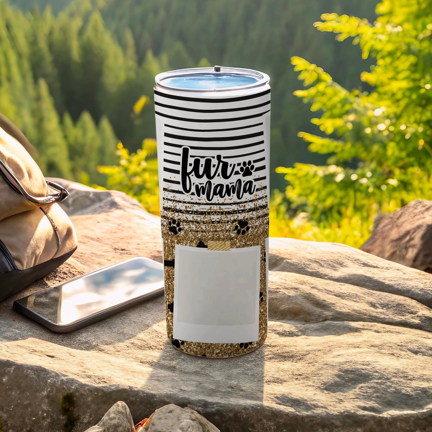 White tumbler with "Fur Mama" text, paw prints, and glitter, resting outdoors.