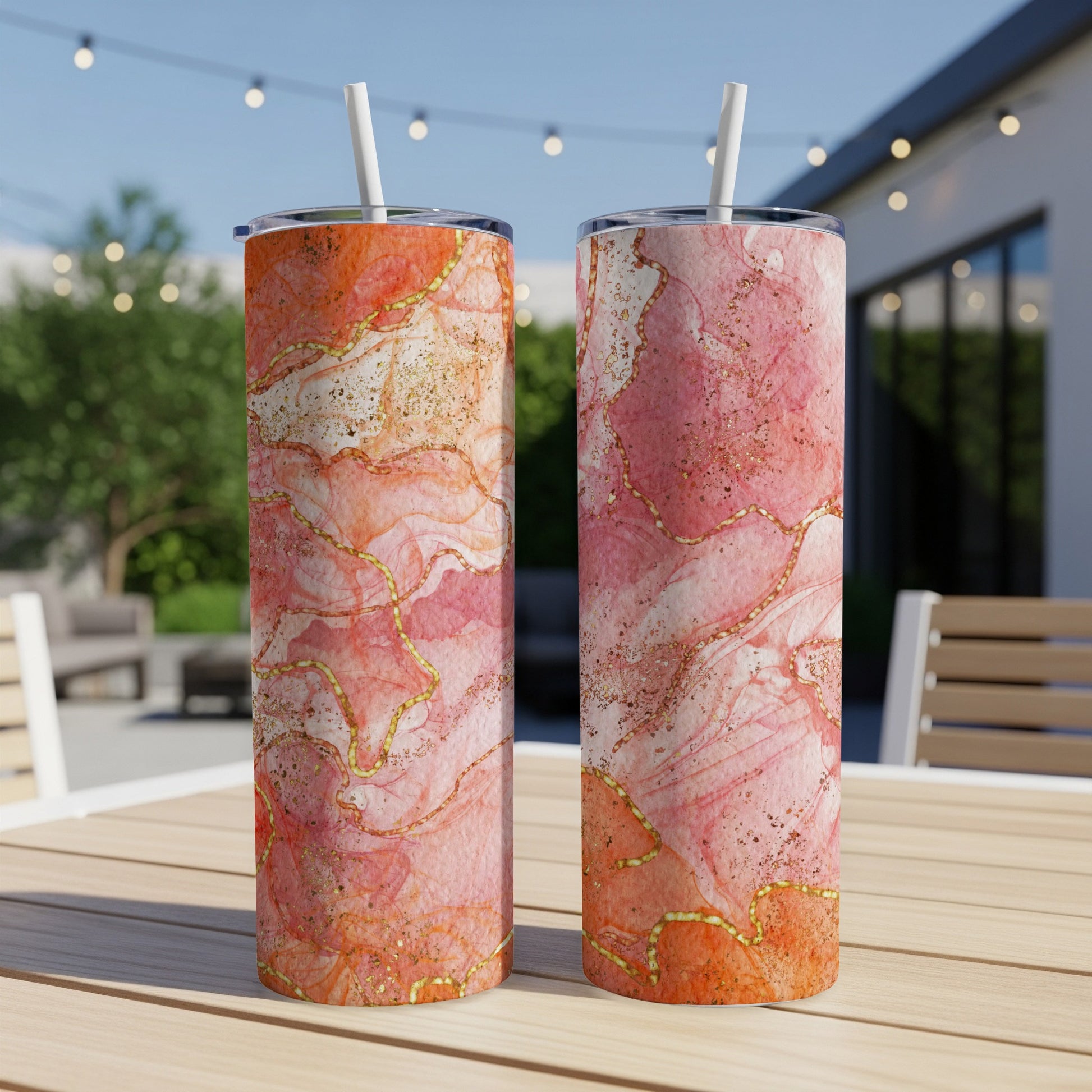Two pink and gold marbled tumblers with straws on a wooden table.