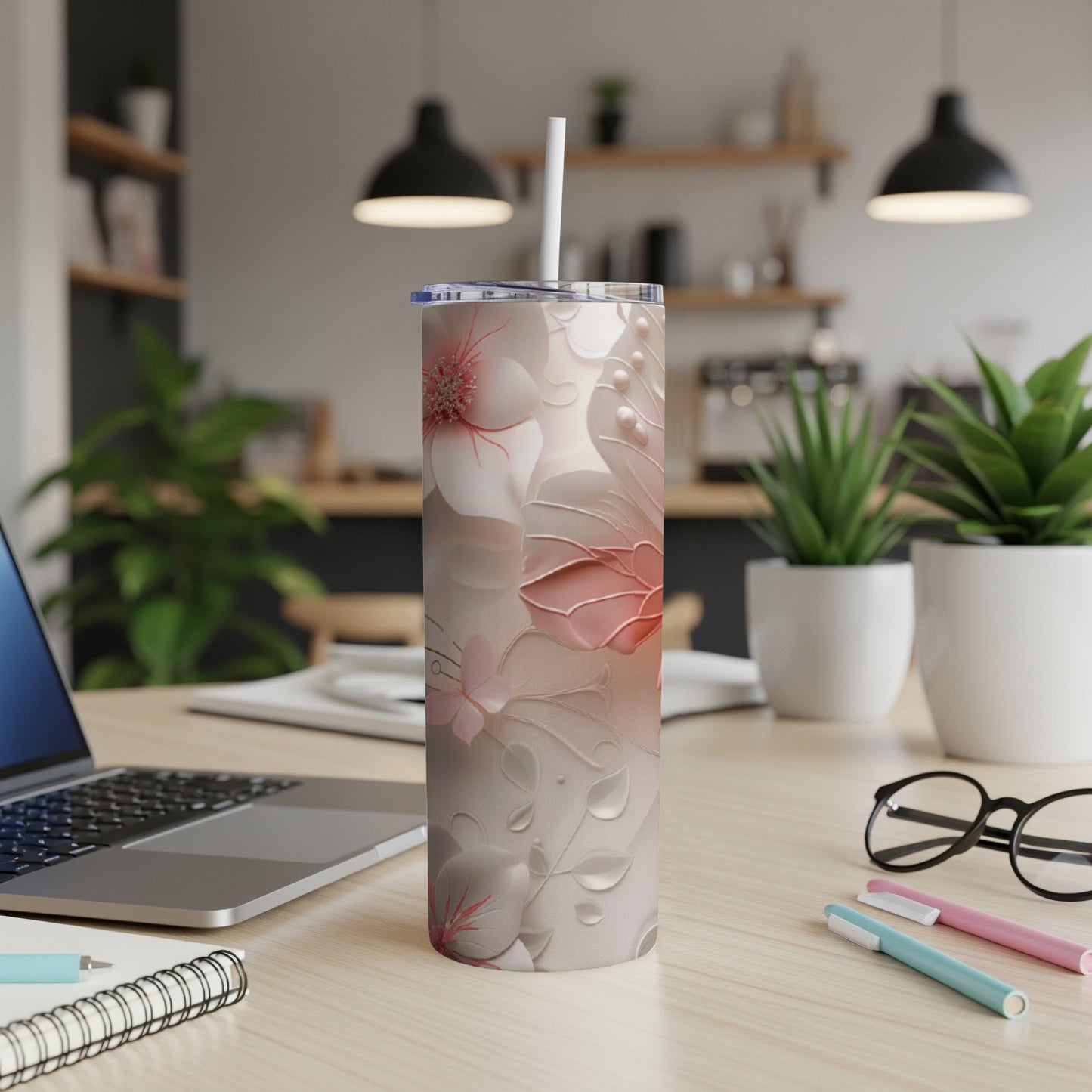 Floral tumbler with straw on a desk with laptop and pens.