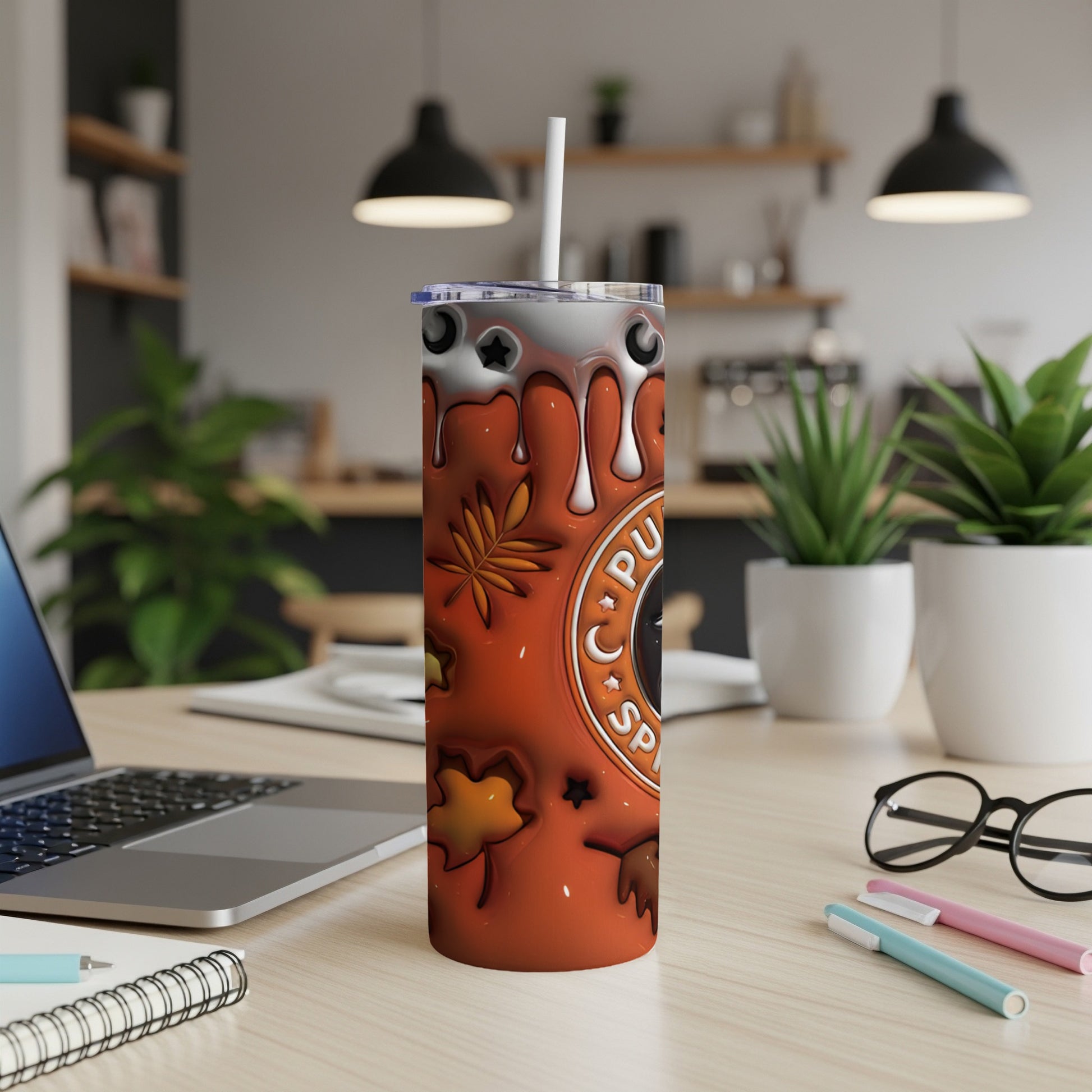 Orange tumbler with pumpkin spice and fall leaf design, on a desk.
