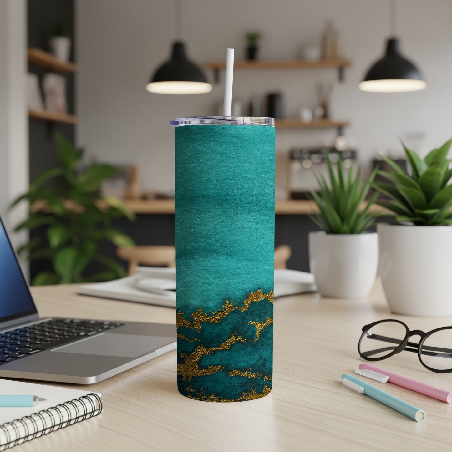 Teal and gold abstract pattern tumbler with straw on desk.