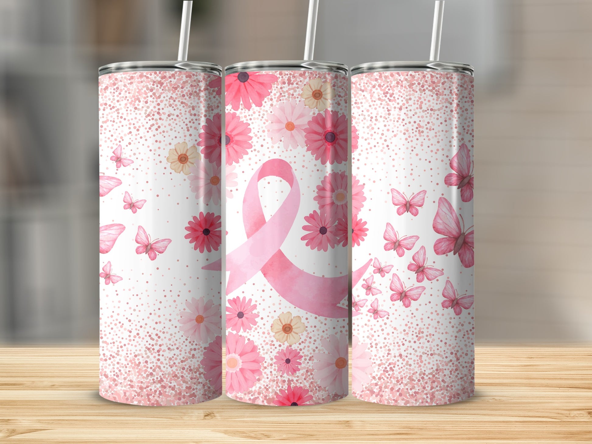 Pink ribbon, flowers, and butterflies adorn three tumblers on a wooden surface.