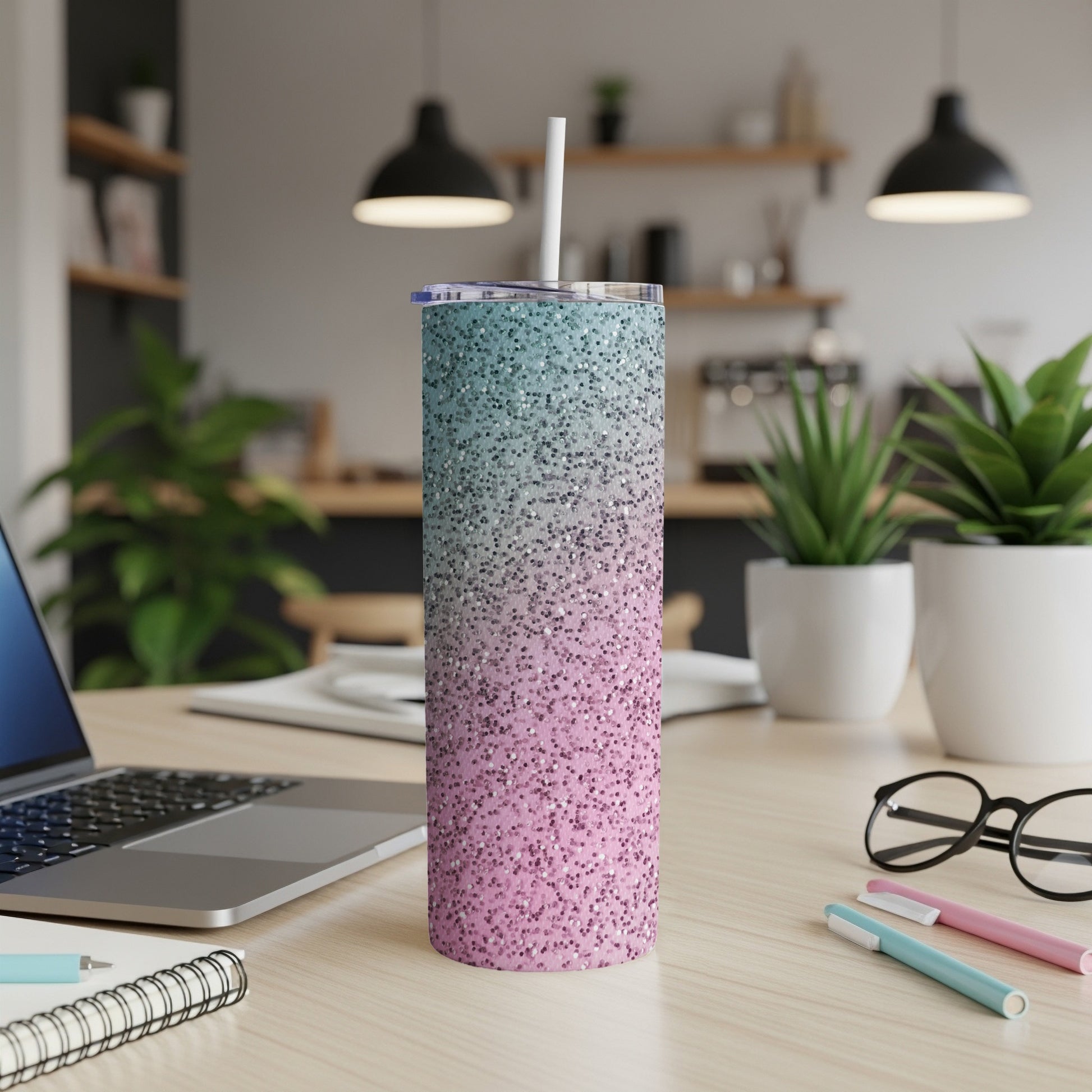 Glitter tumbler with a straw on a desk next to a laptop.