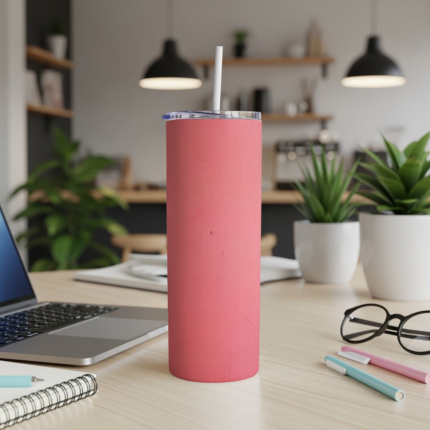 Coral pink tumbler with white straw on a wooden desk with laptop.