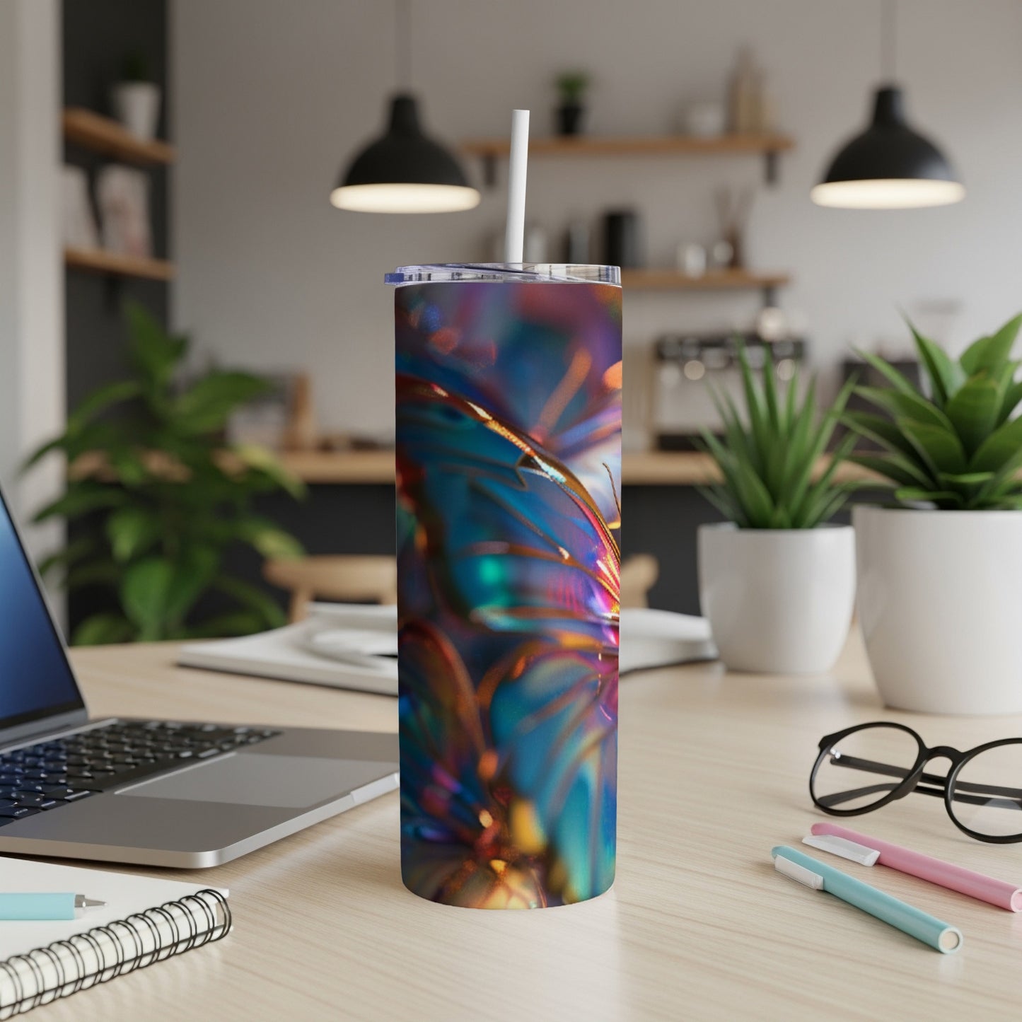 Iridescent metallic tumbler with straw on desk with laptop and pens.