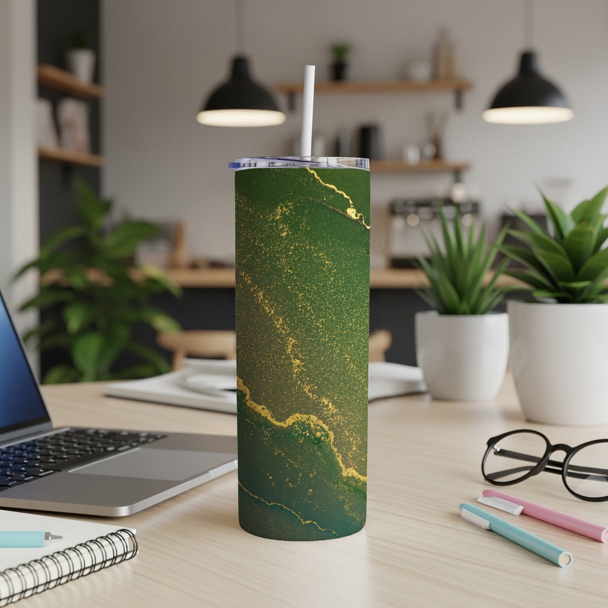 Green and gold marble tumbler with white straw on a desk.