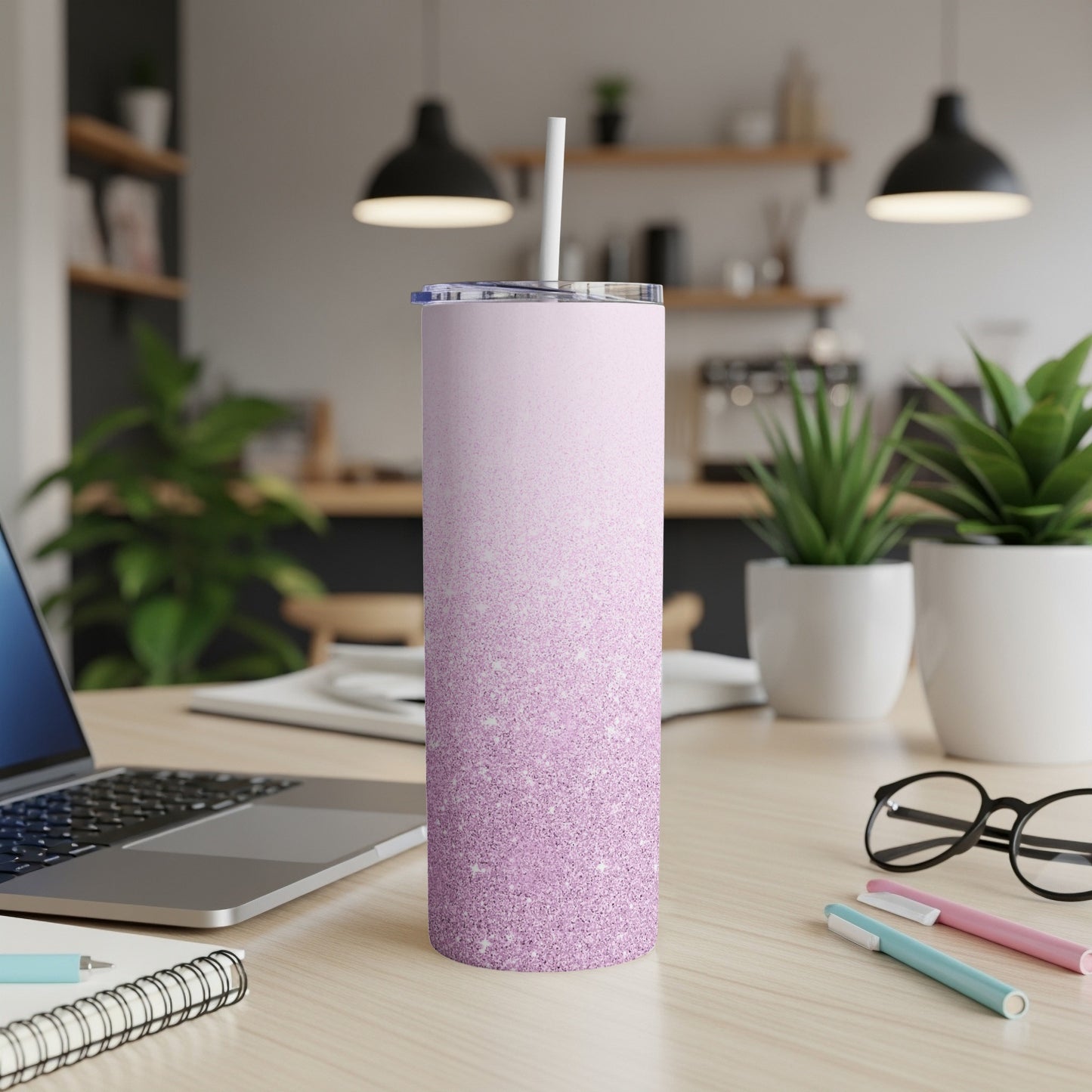 Pink glitter ombre tumbler with straw on a desk with a laptop.