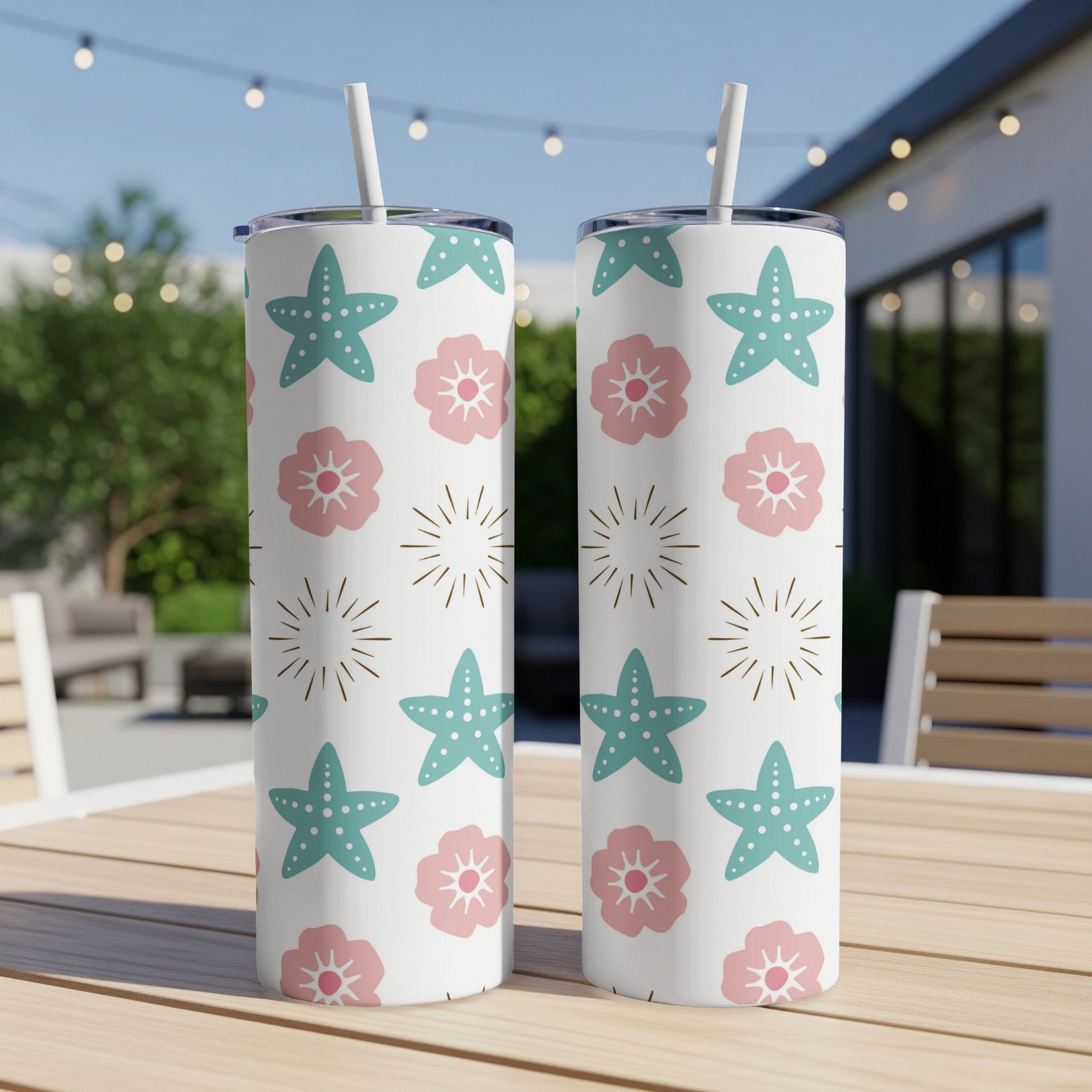 Two tall tumblers with a starfish and floral pattern sit on a wooden table outdoors.
