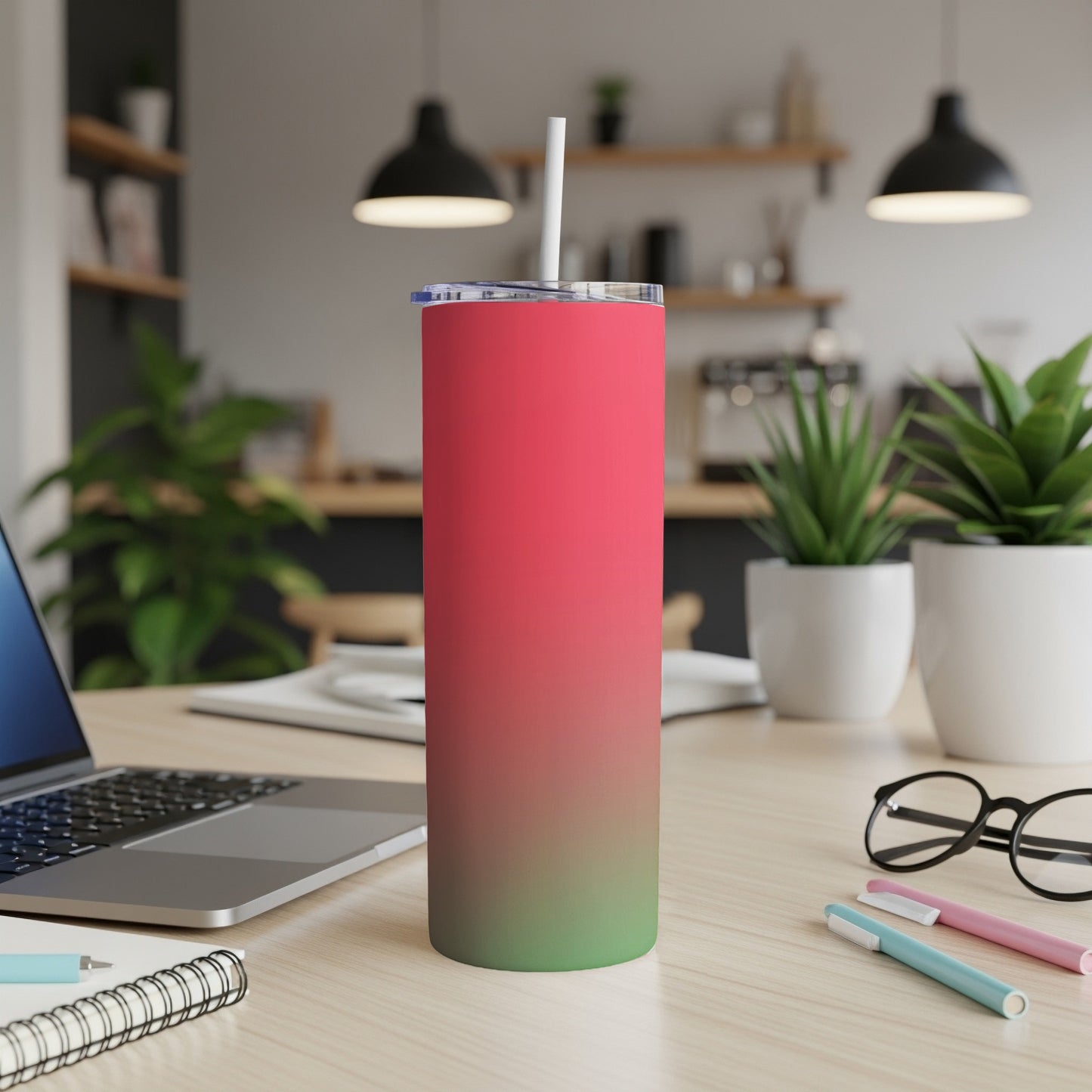 Tall pink and green gradient tumbler with straw on desk next to laptop and glasses.