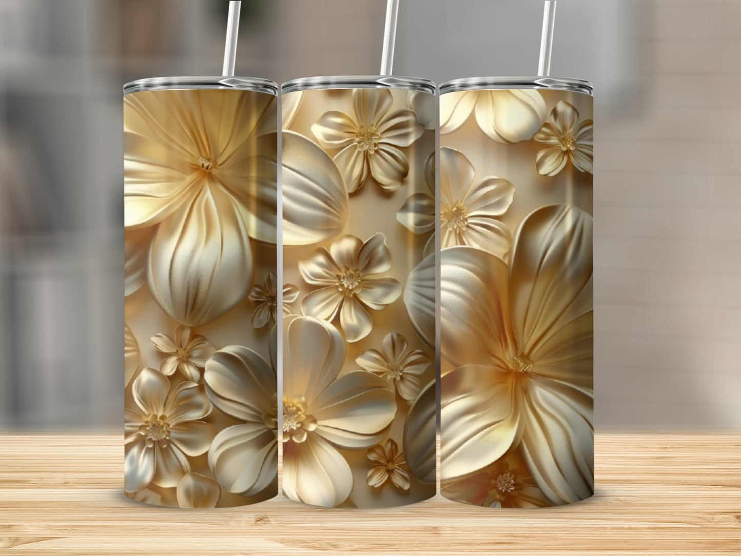 Three gold tumblers with embossed floral designs on a wooden surface.