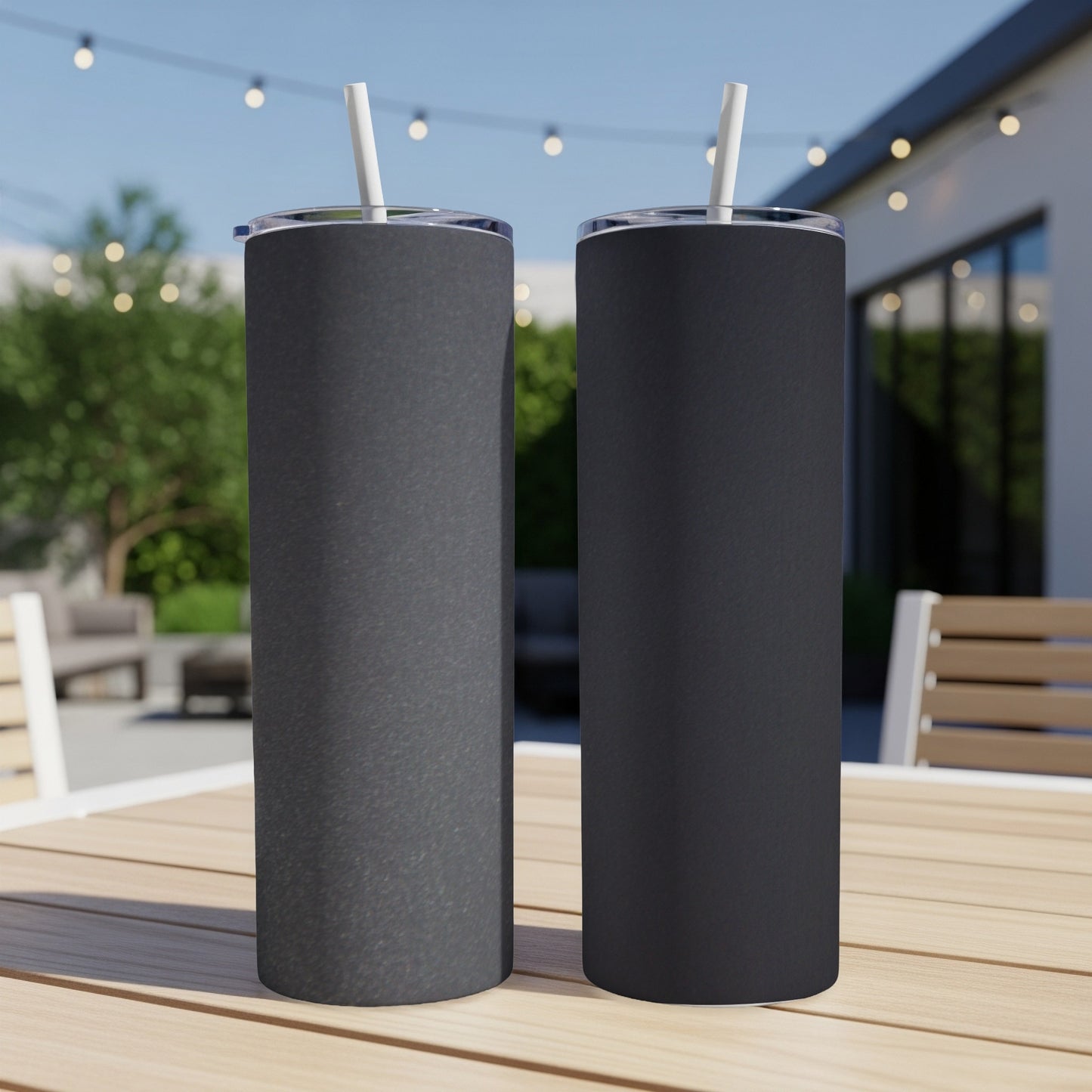 Two dark grey tumblers with straws on a wooden table outdoors.